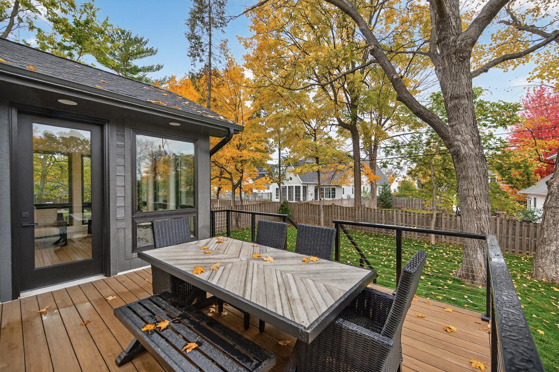 Furnished wooden deck with an outdoor dining table, wicker chairs, and autumn trees.