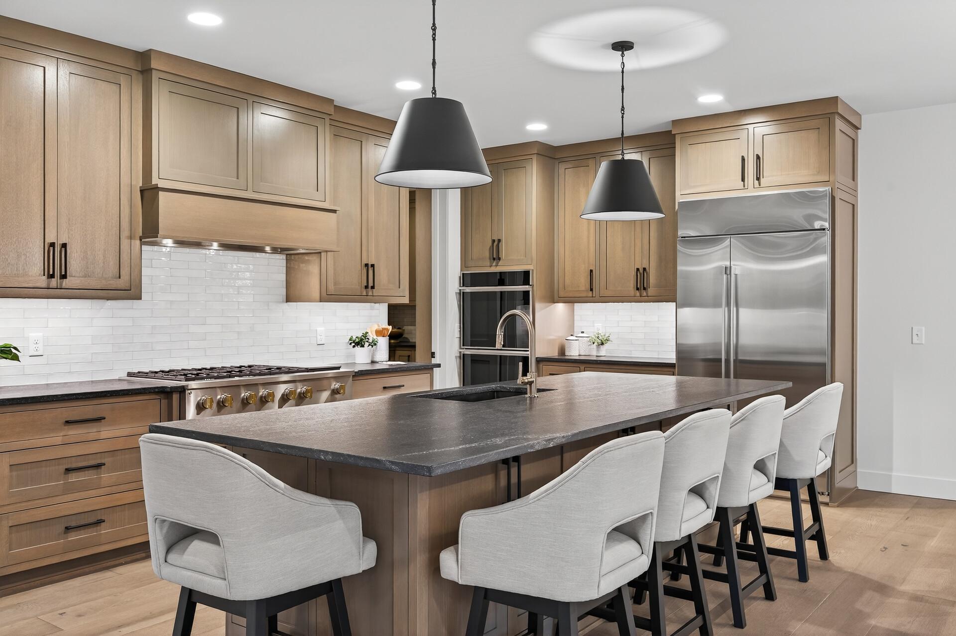 Kitchen with light wood cabinets, stainless steel appliances, and a large island lined with upholstered stools.