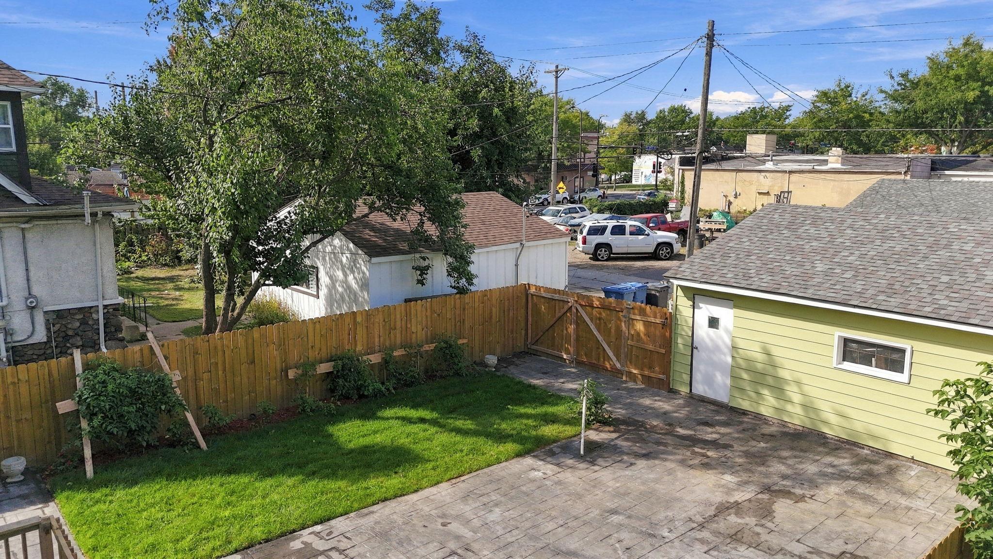 Fenced backyard with a green lawn, paved patio, and light-green detached garage.