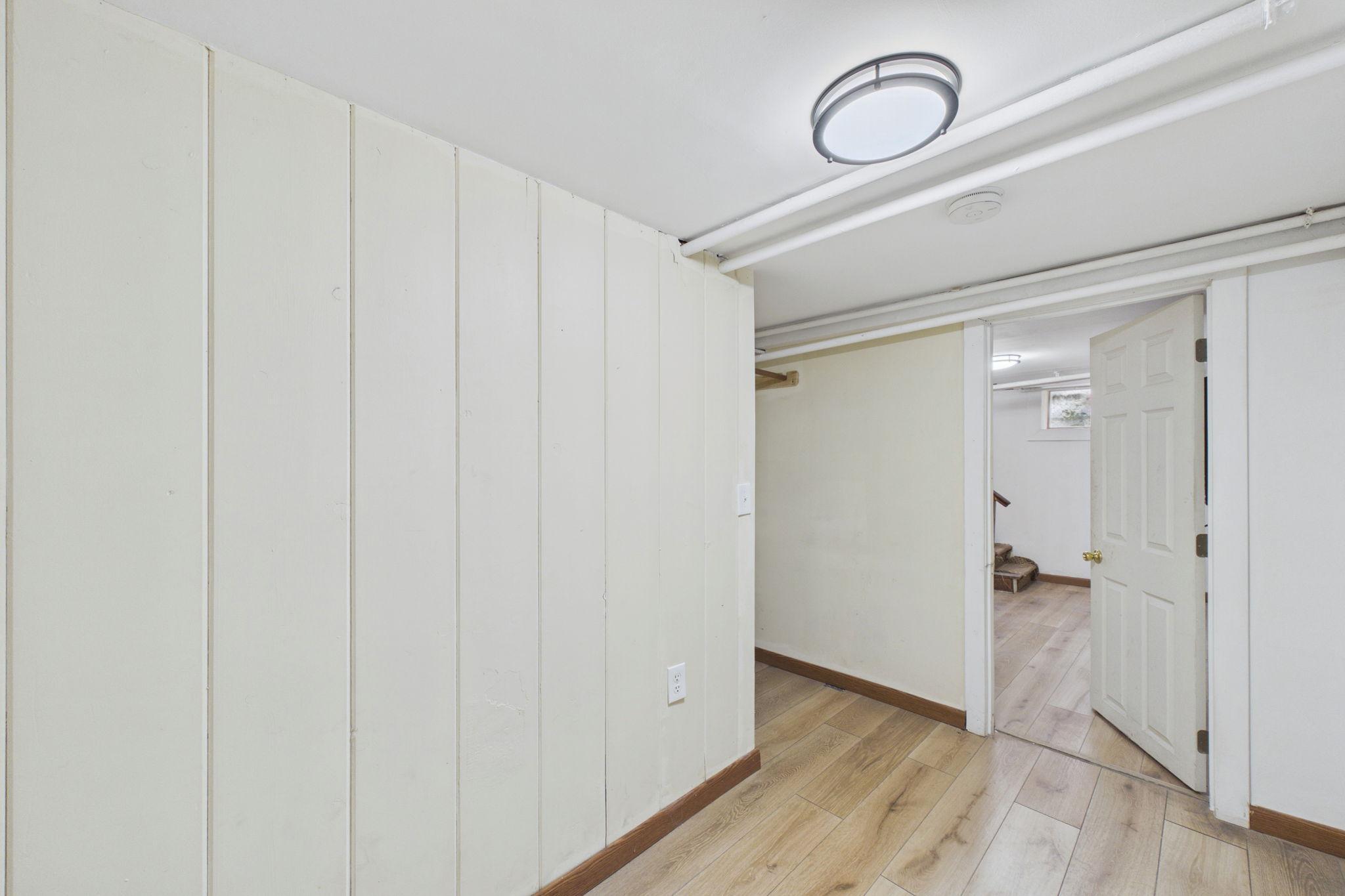 Empty basement hallway with paneled walls, wood-look flooring, and an open doorway.