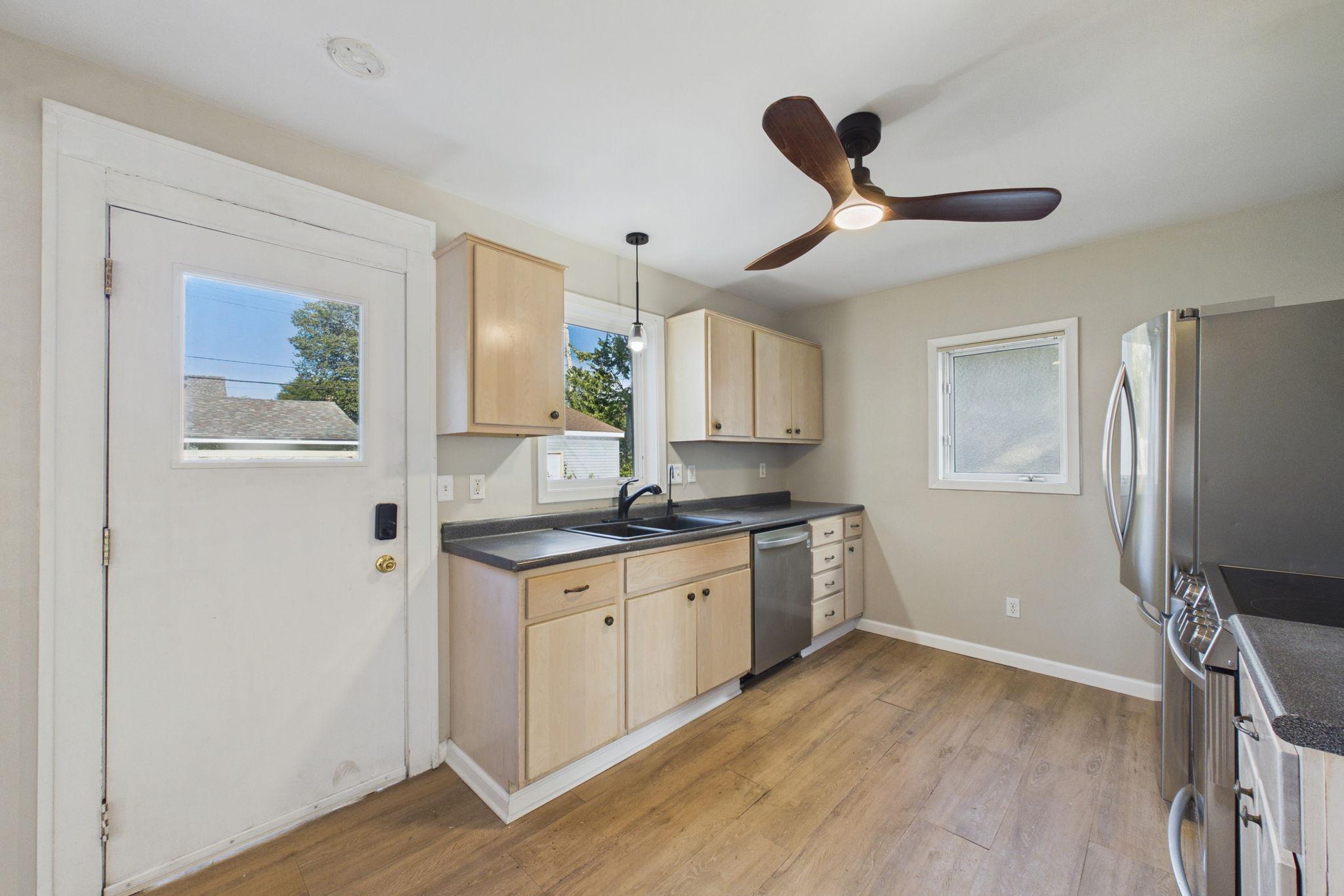 Kitchen with light wood cabinets, dark counters, stainless appliances, and a ceiling fan.