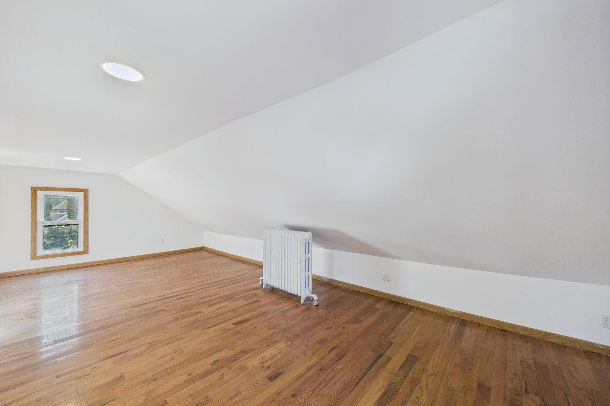 Empty upper-floor room with a sloped ceiling, hardwood floors, and a freestanding radiator.