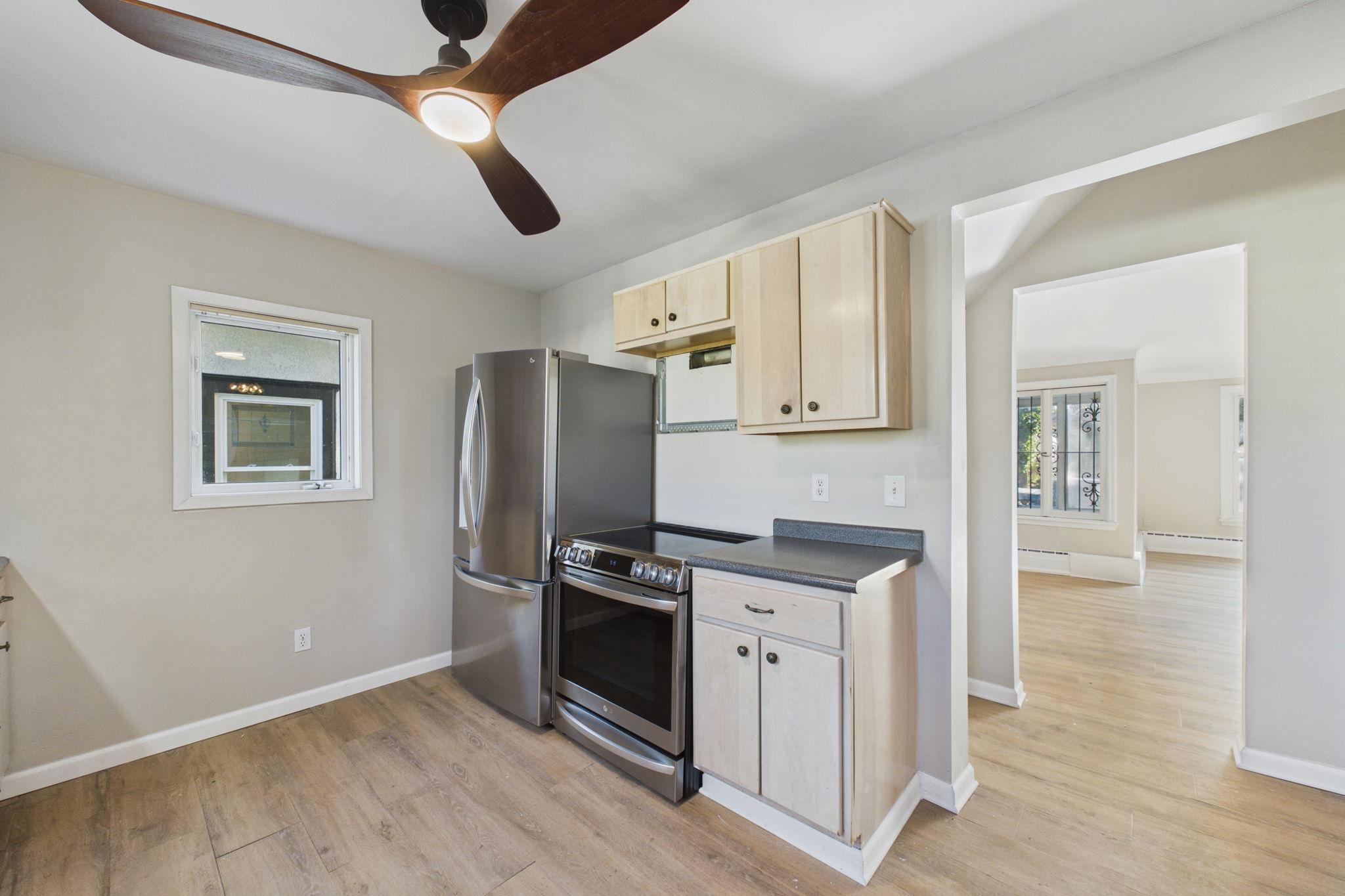 Kitchen with stainless steel appliances, light wood cabinets, and an open doorway to the adjoining room.