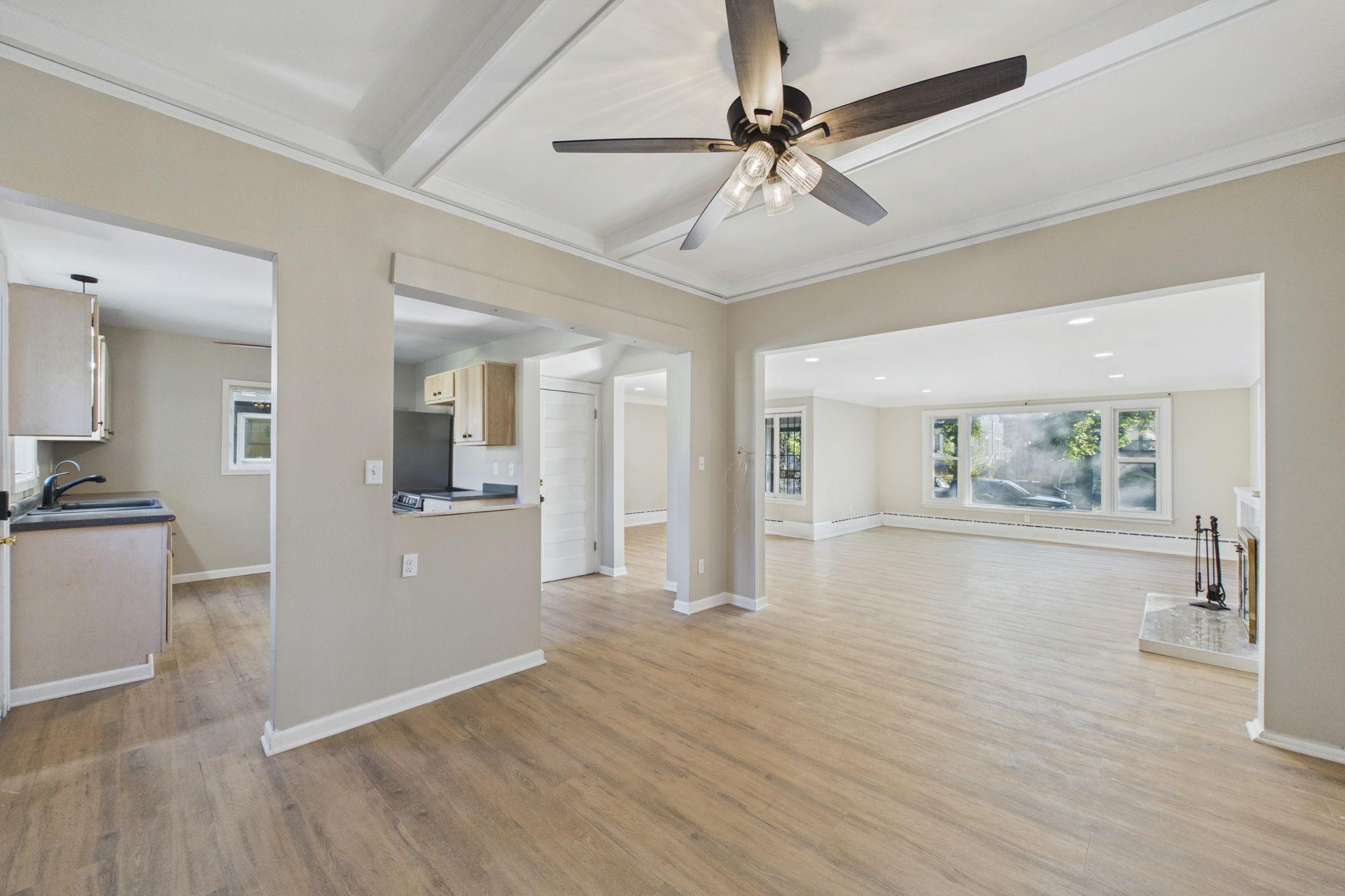 Open-plan living area with wood-look floors, coffered ceiling, kitchen, and fireplace.