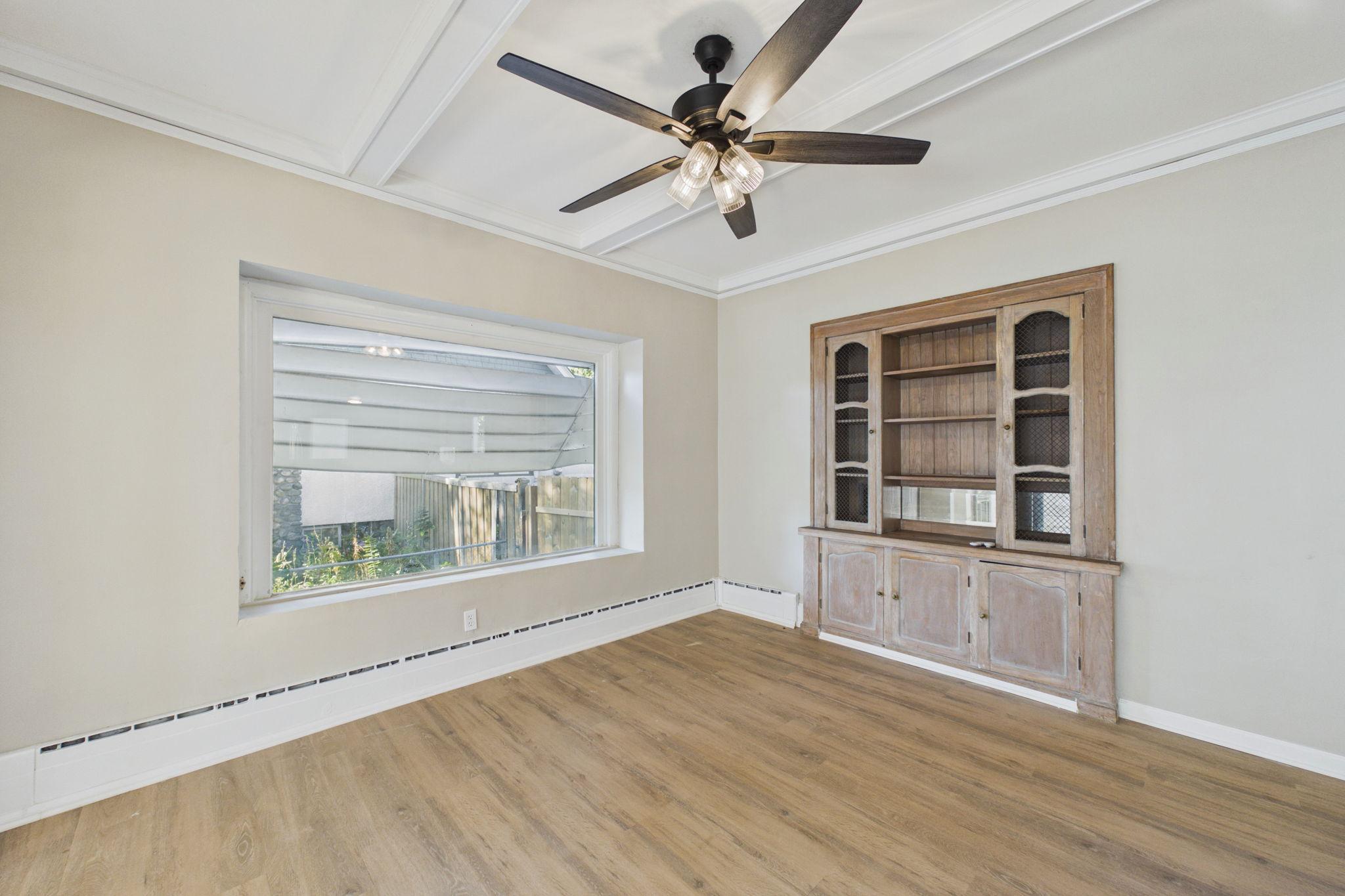 Empty room with wood floors, a built-in hutch, large window, and coffered ceiling.