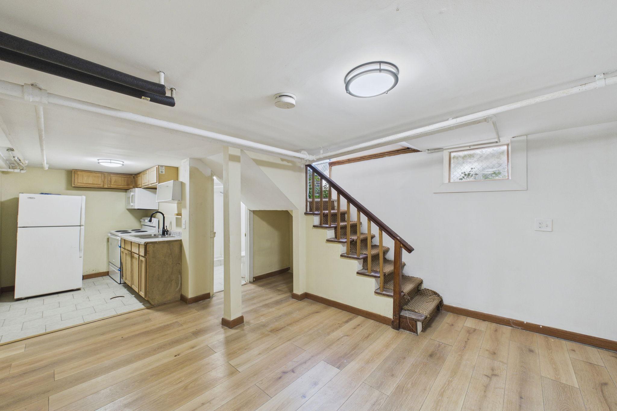 Basement with a compact kitchenette and carpeted stairs with a dark wood railing.