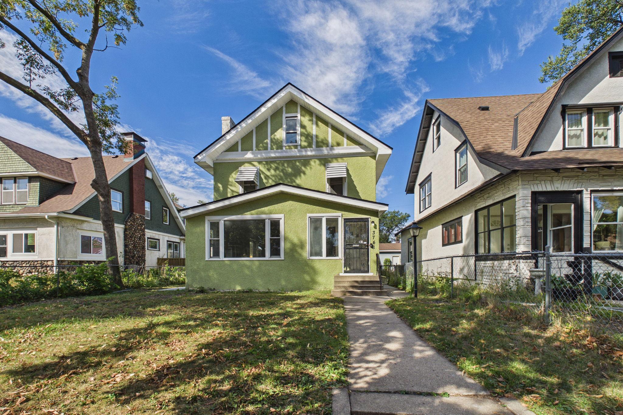 Green two-story house with white trim, a steep front gable, and a walkway to the entrance.