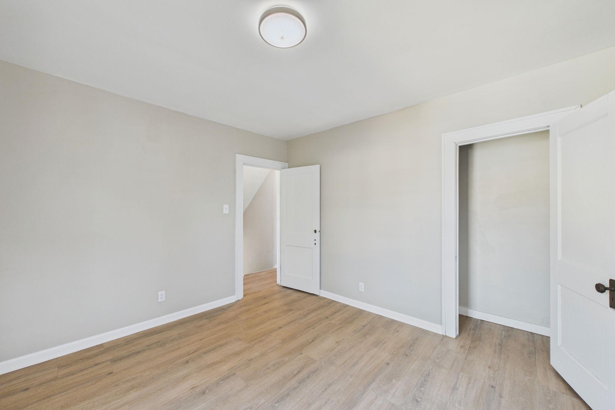 Vacant room with wood-look flooring, gray walls, and two open doorways.