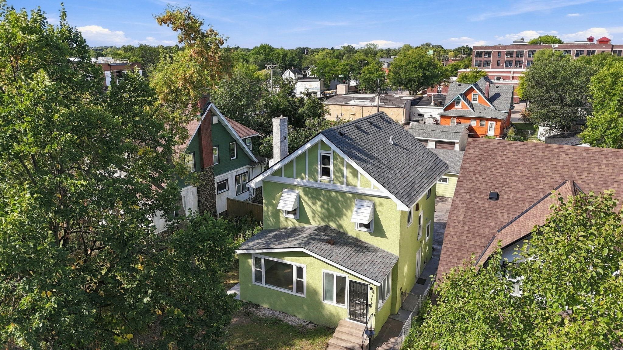Lime-green two-story house with white trim, viewed from above among leafy trees and neighborhood rooftops.