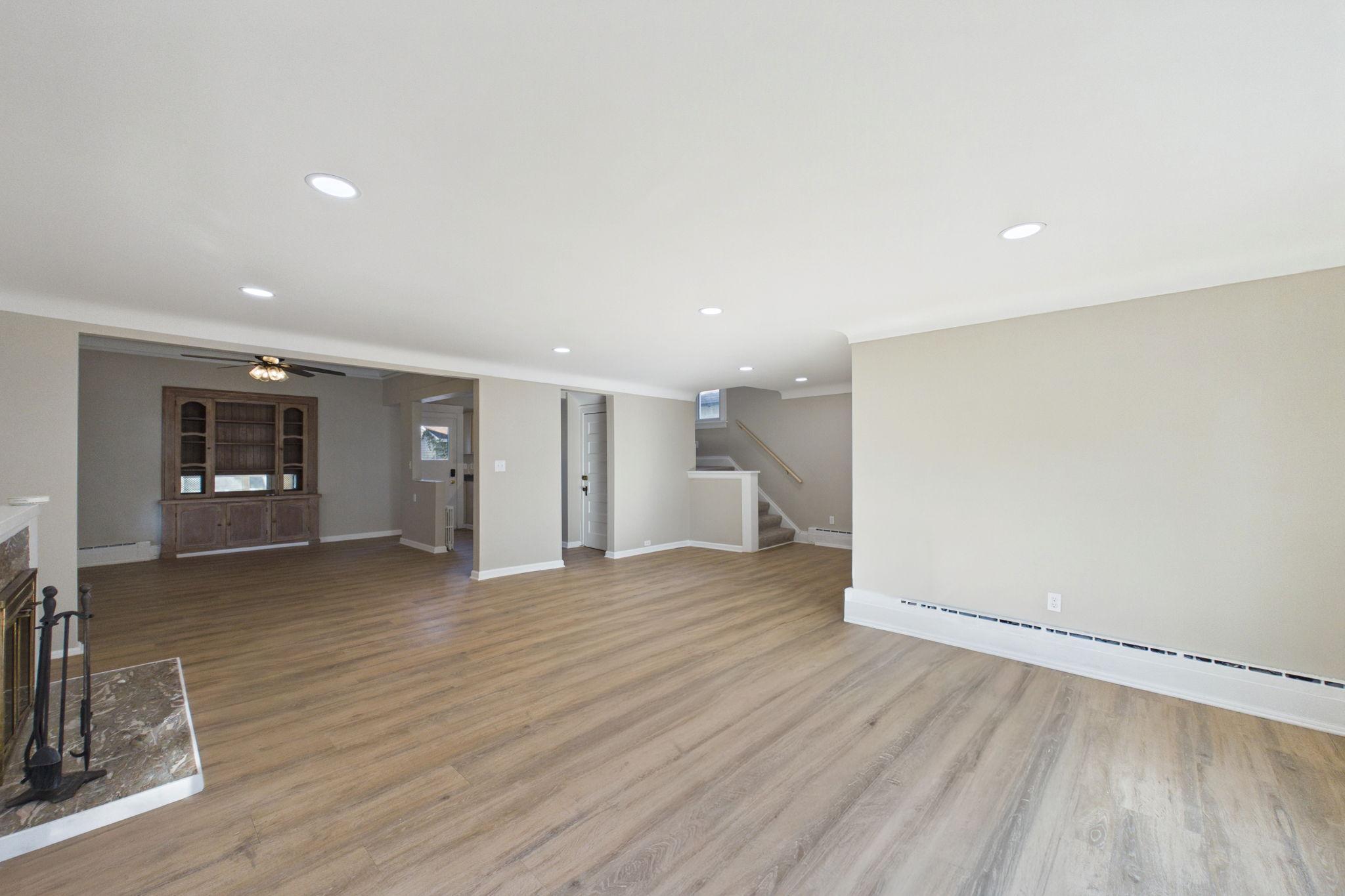 Empty living area with wood-look floors, built-in cabinetry, fireplace, and stairs.