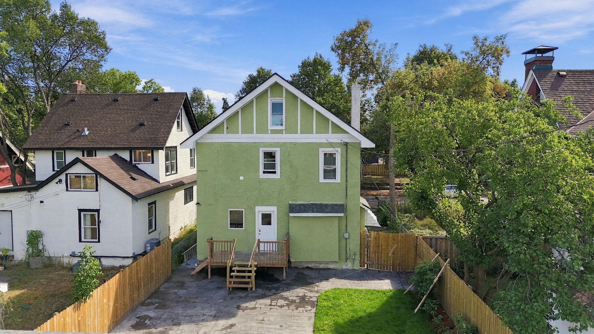 Rear of a green two-story house with a raised deck, paved patio, and fenced yard.