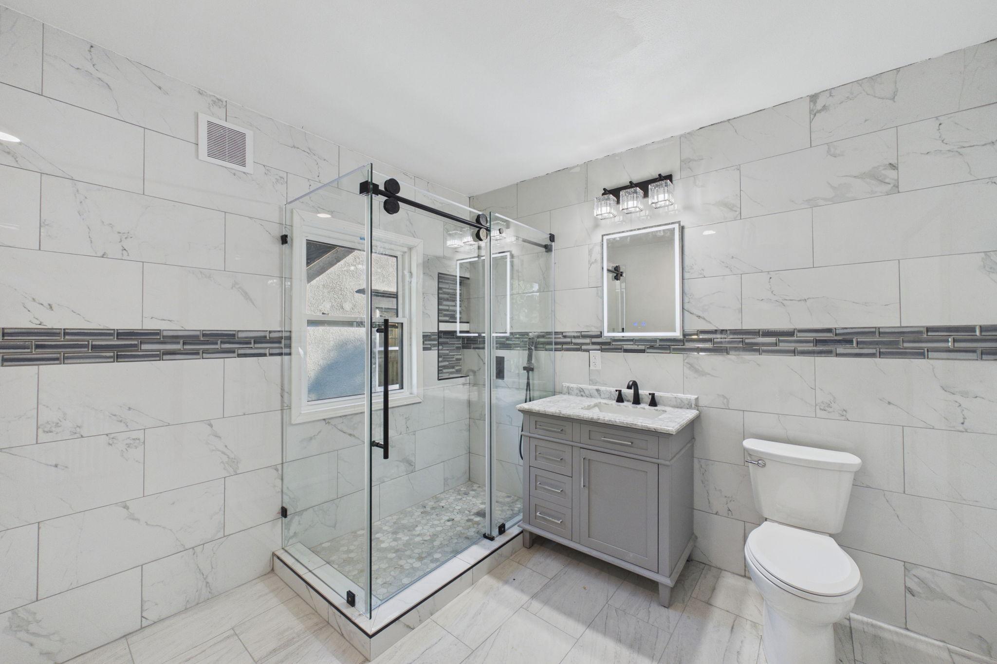 Bathroom with a glass walk-in shower, gray vanity, and marble-look tile.