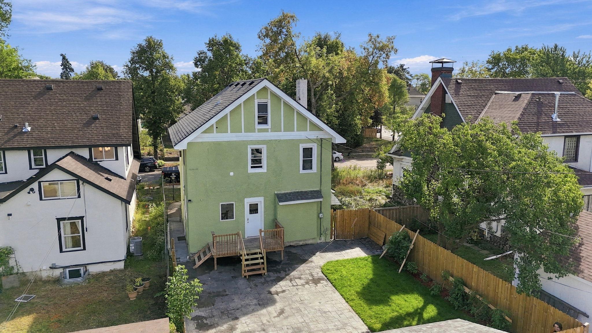 Rear of a green gabled house with a raised deck, paved patio, and fenced lawn.