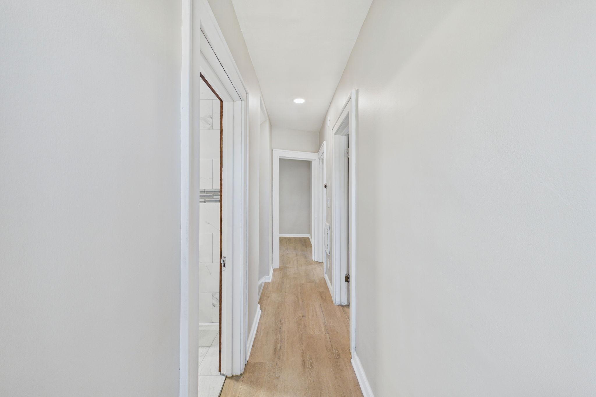 Bright hallway with light wood flooring, white walls, and open doorways.
