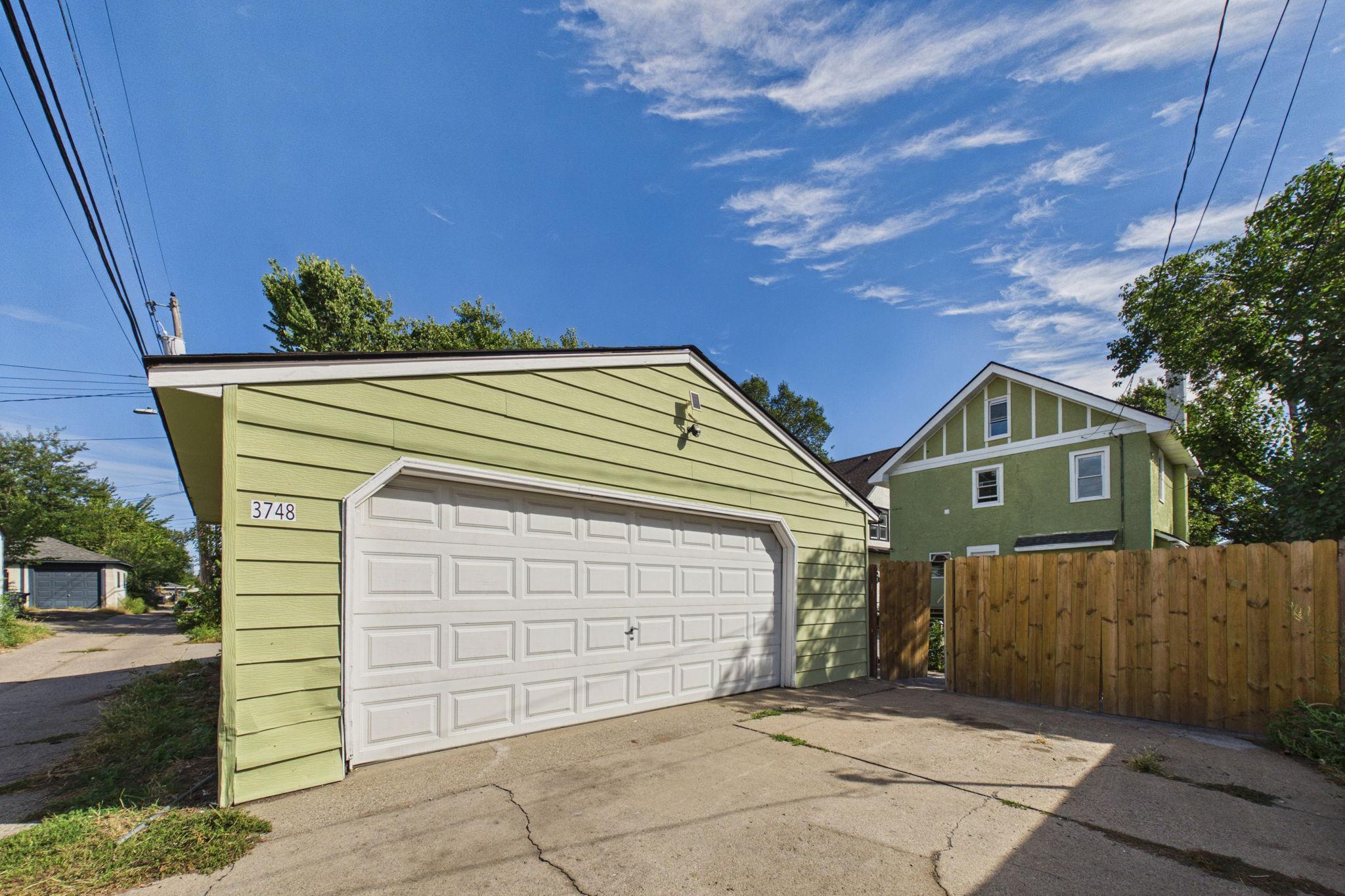 Pale green garage with a large white paneled door, driveway, and wooden fence.