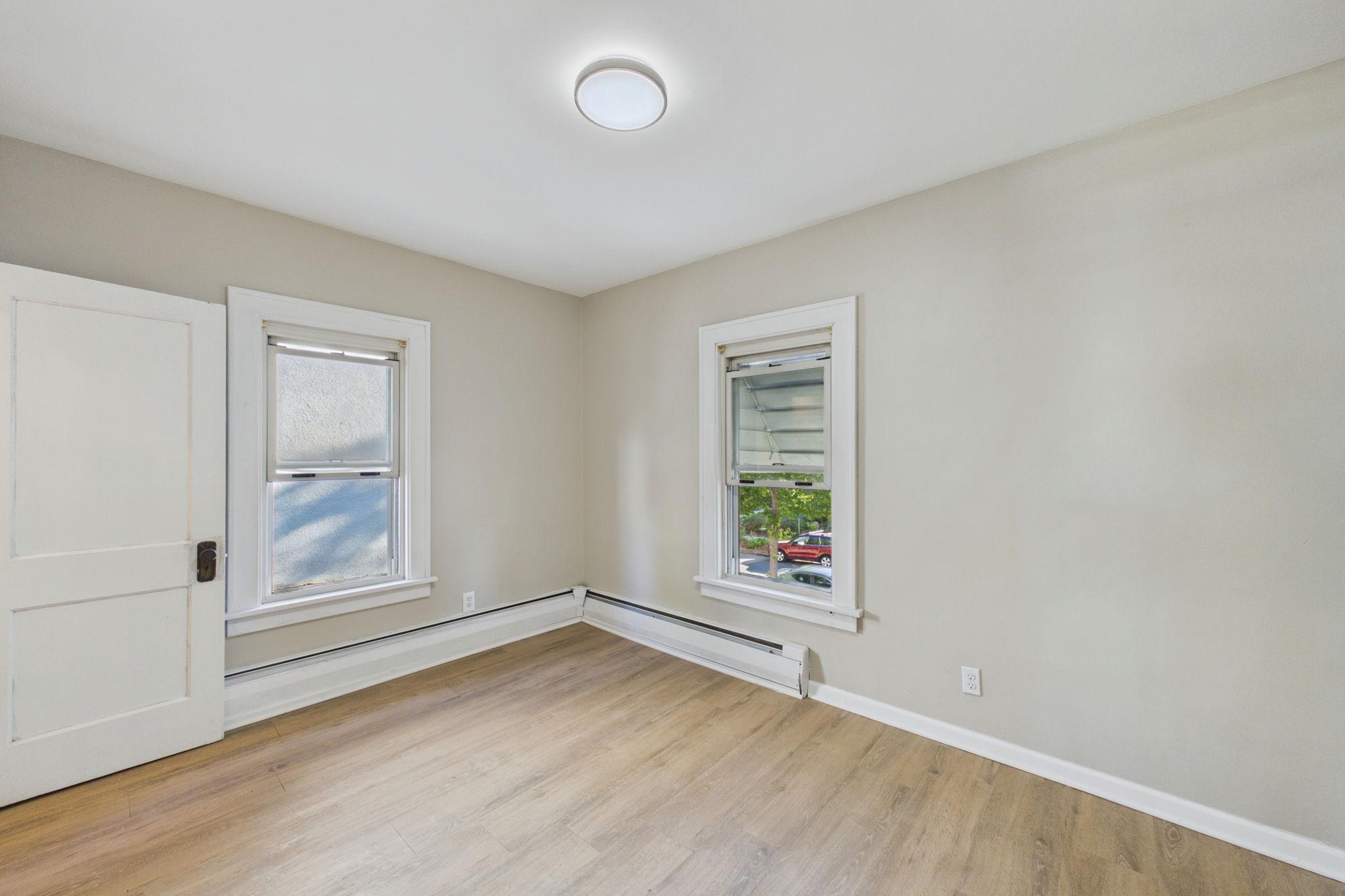 Vacant room with light wood floors, two windows, and baseboard heating.
