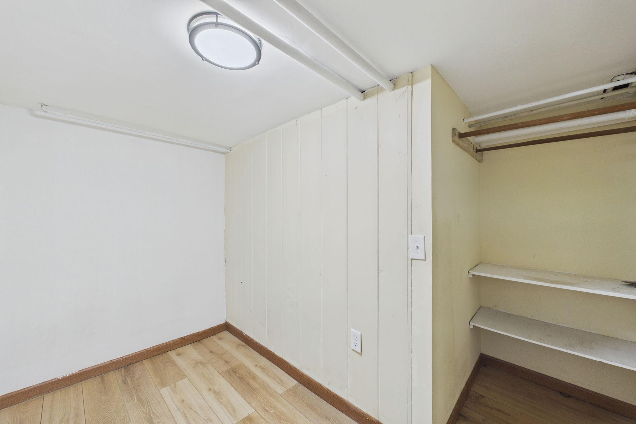 Small empty room with an open closet, hanging rods, shelves, and light wood-look flooring.