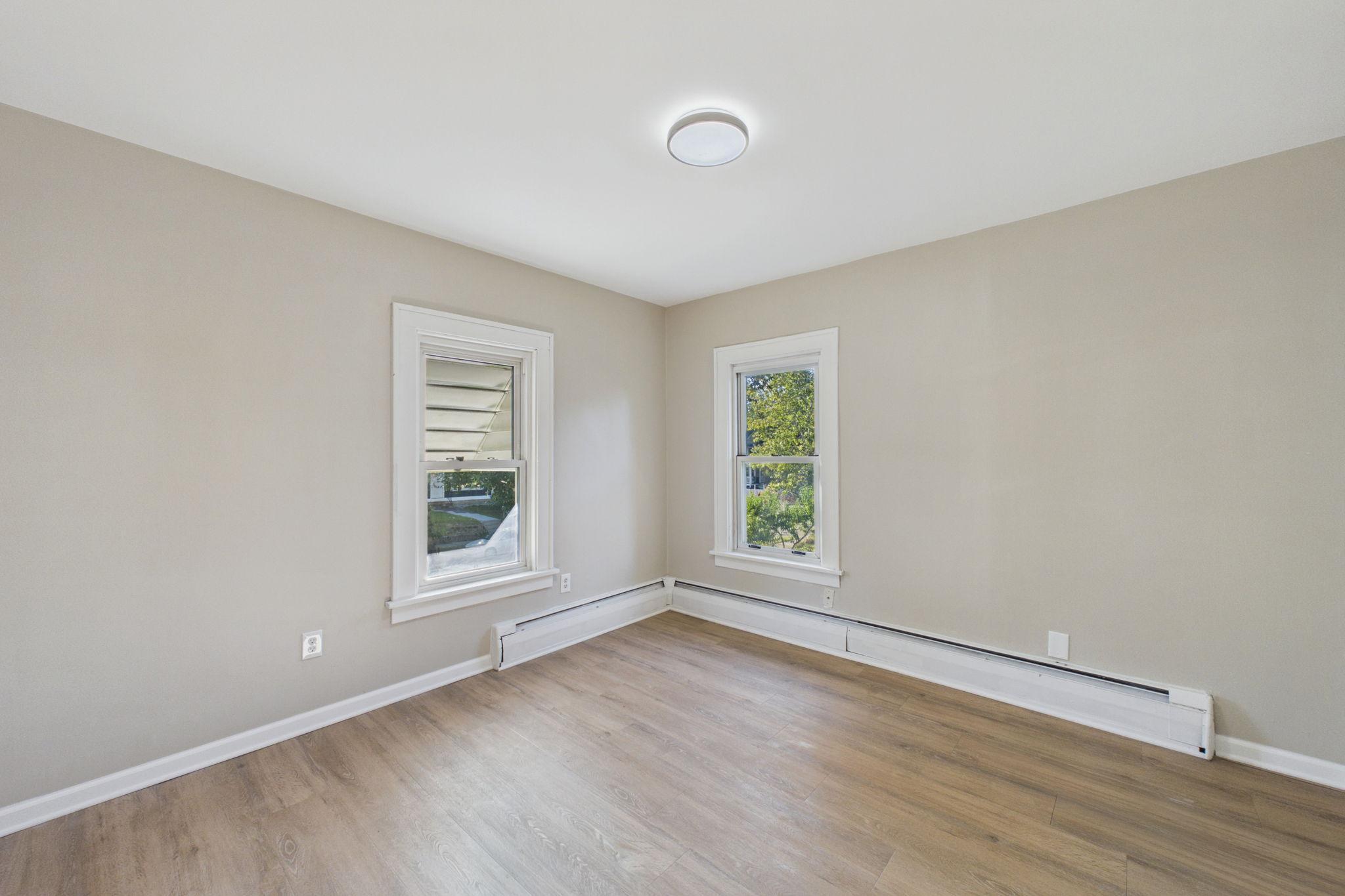 Empty room with wood-look flooring, two windows, and white baseboard heaters.