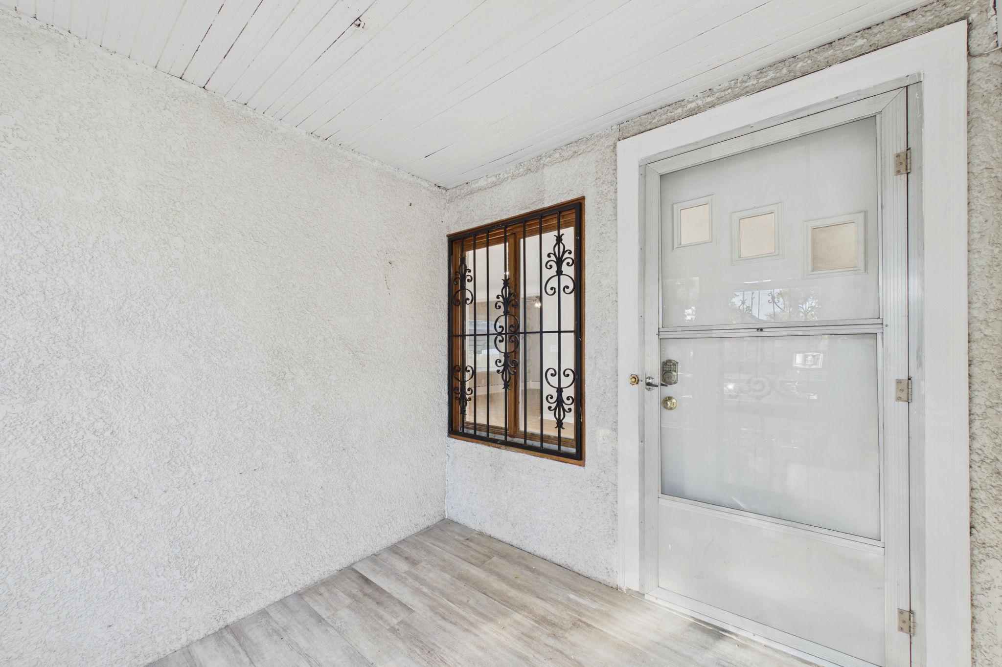Enclosed entry with a white door, decorative window bars, and gray plank flooring.
