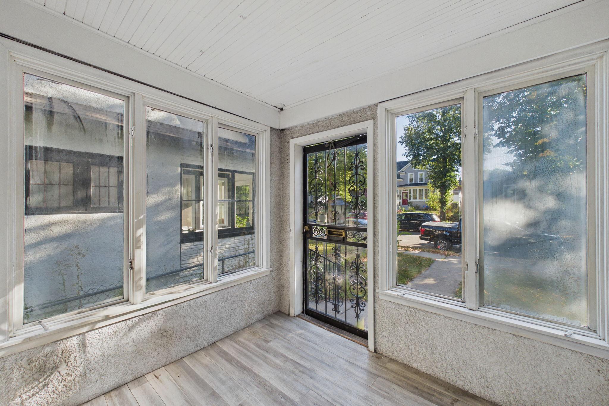 Enclosed front porch with broad windows and an ornate black security door facing the street.