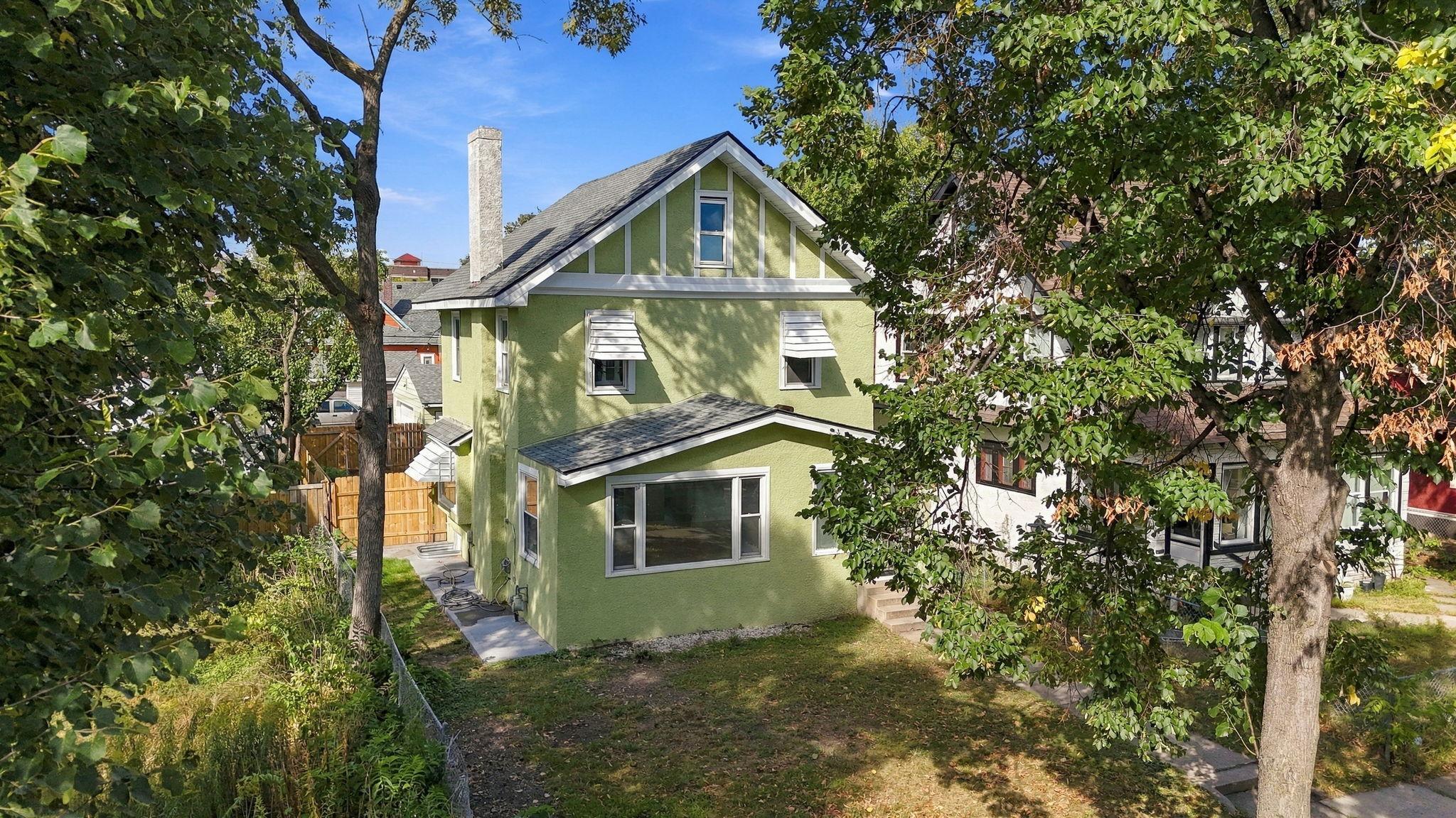 Green stucco house with a steep gabled roof, viewed from above through leafy trees.