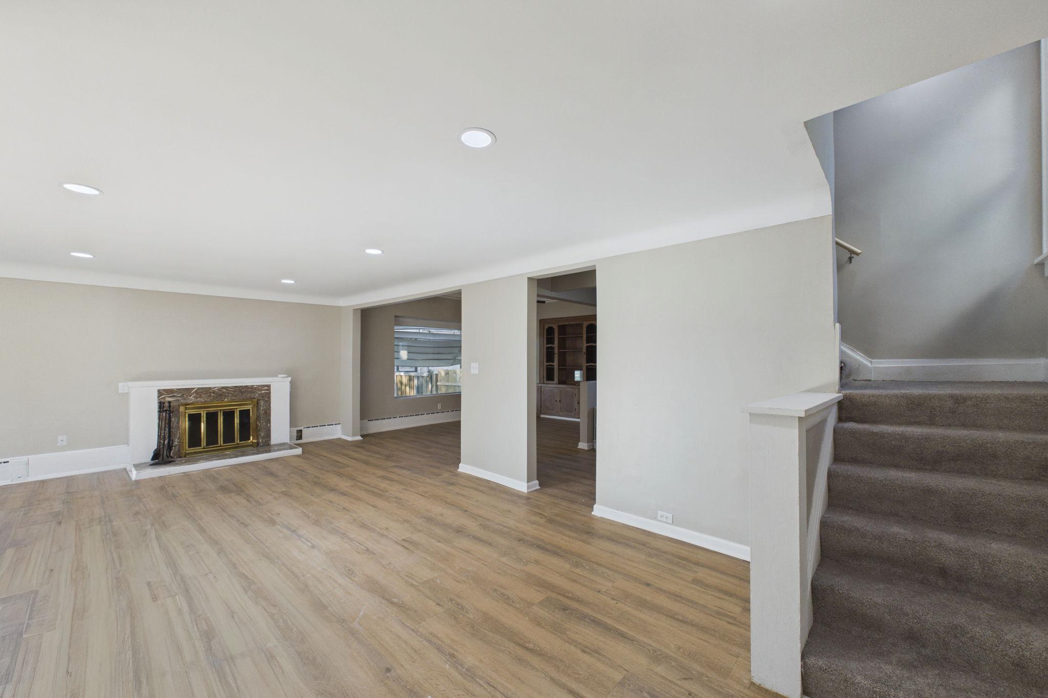 Vacant living room with wood-look flooring, a fireplace, and carpeted stairs.