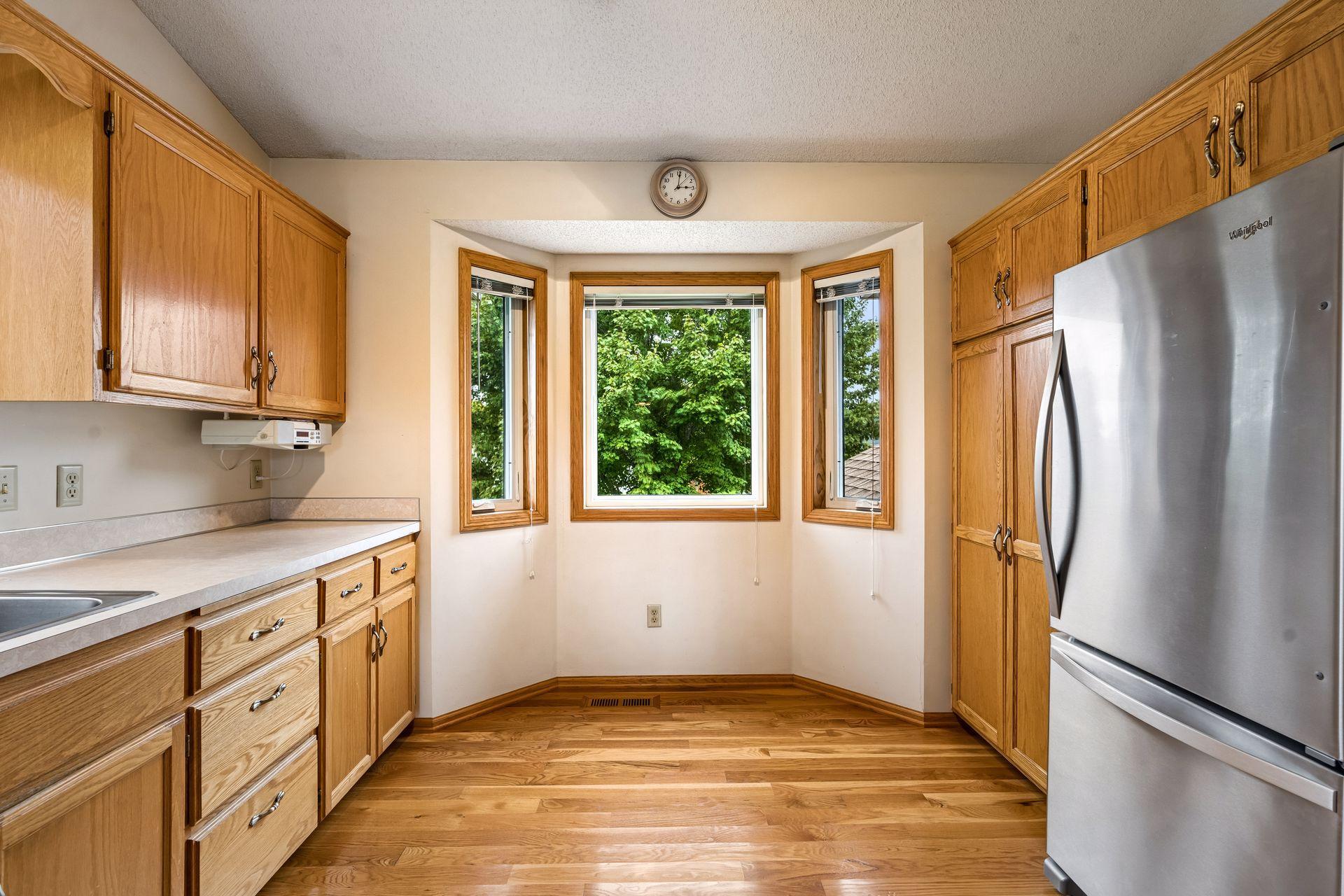 Kitchen with oak cabinets and hardwood floors, centered on a three-window bay overlooking trees.