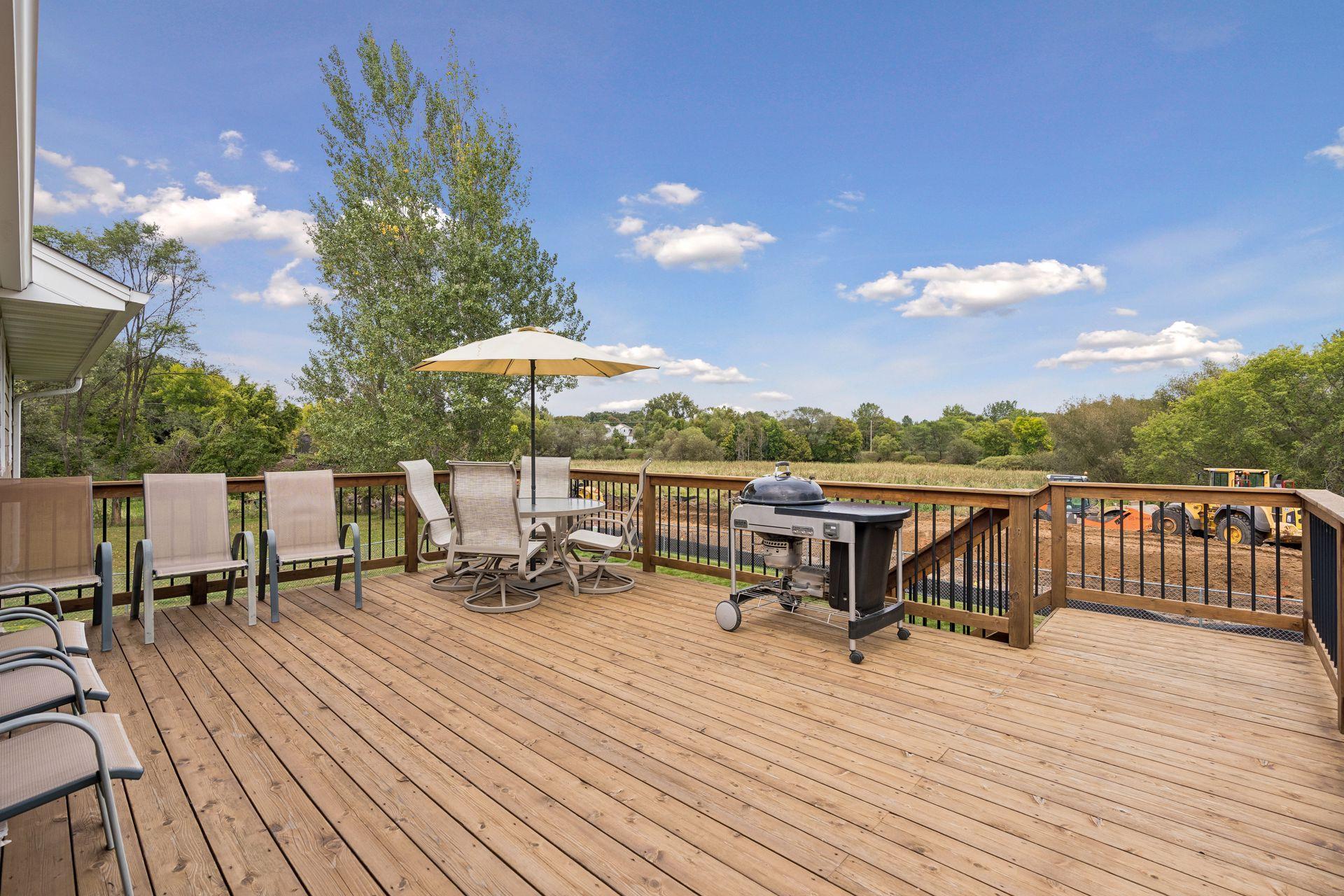 Wooden deck with patio seating, umbrella, and grill overlooking a tree-lined field.