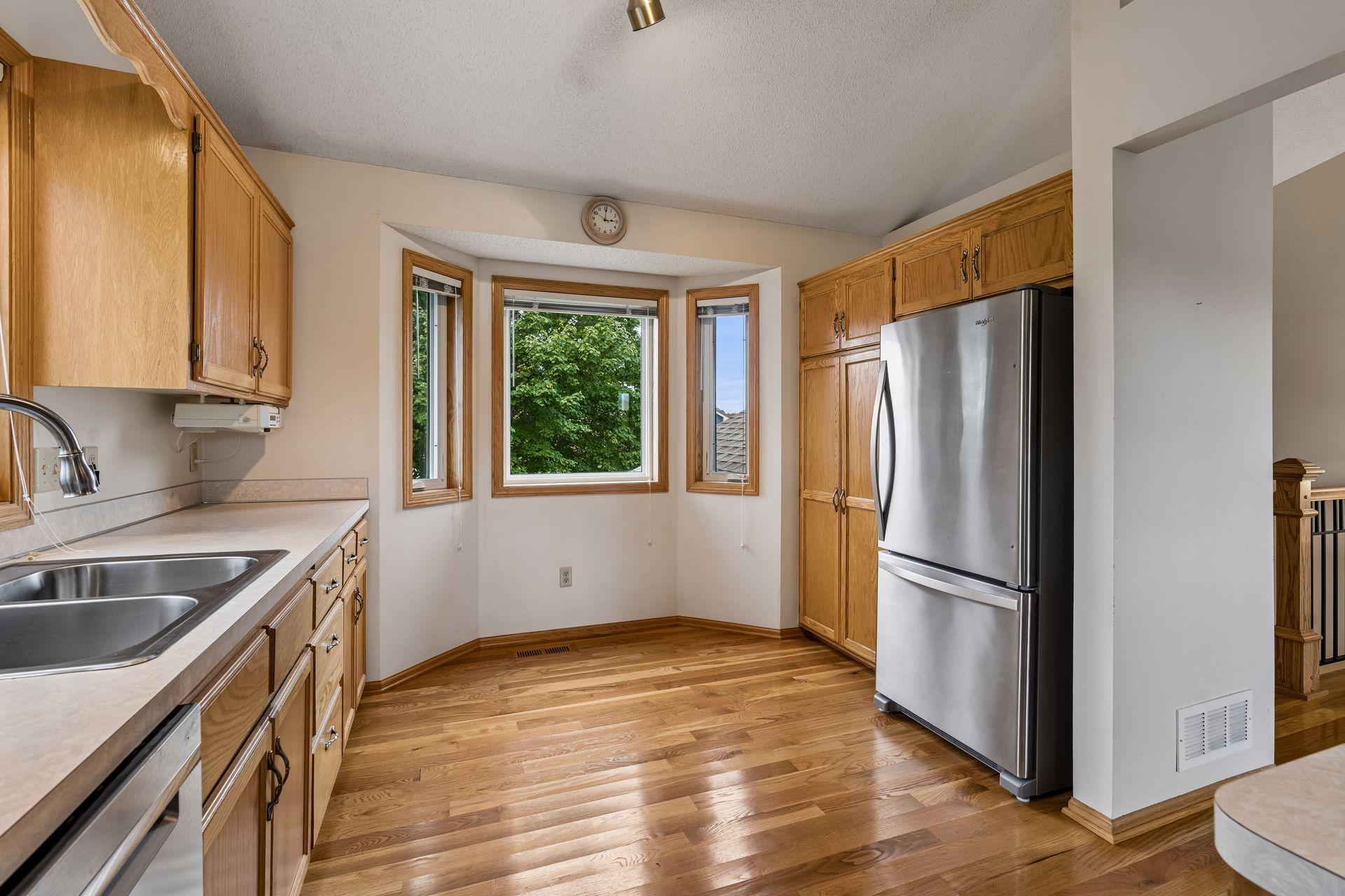 Kitchen with wood cabinets, hardwood floors, stainless steel refrigerator, and a bay window.