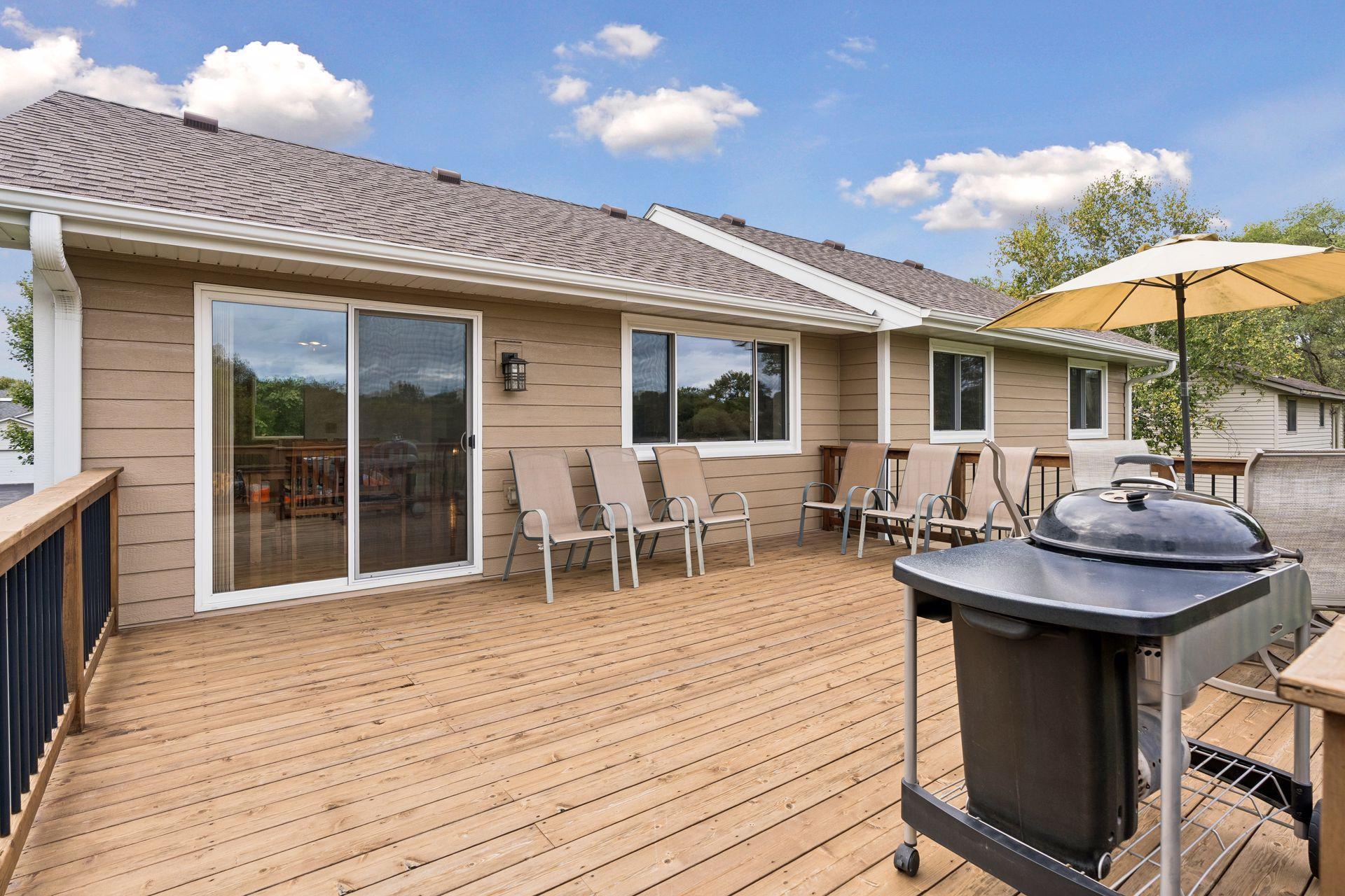 Wooden deck with patio chairs, an umbrella, and barbecue beside the home's sliding doors.