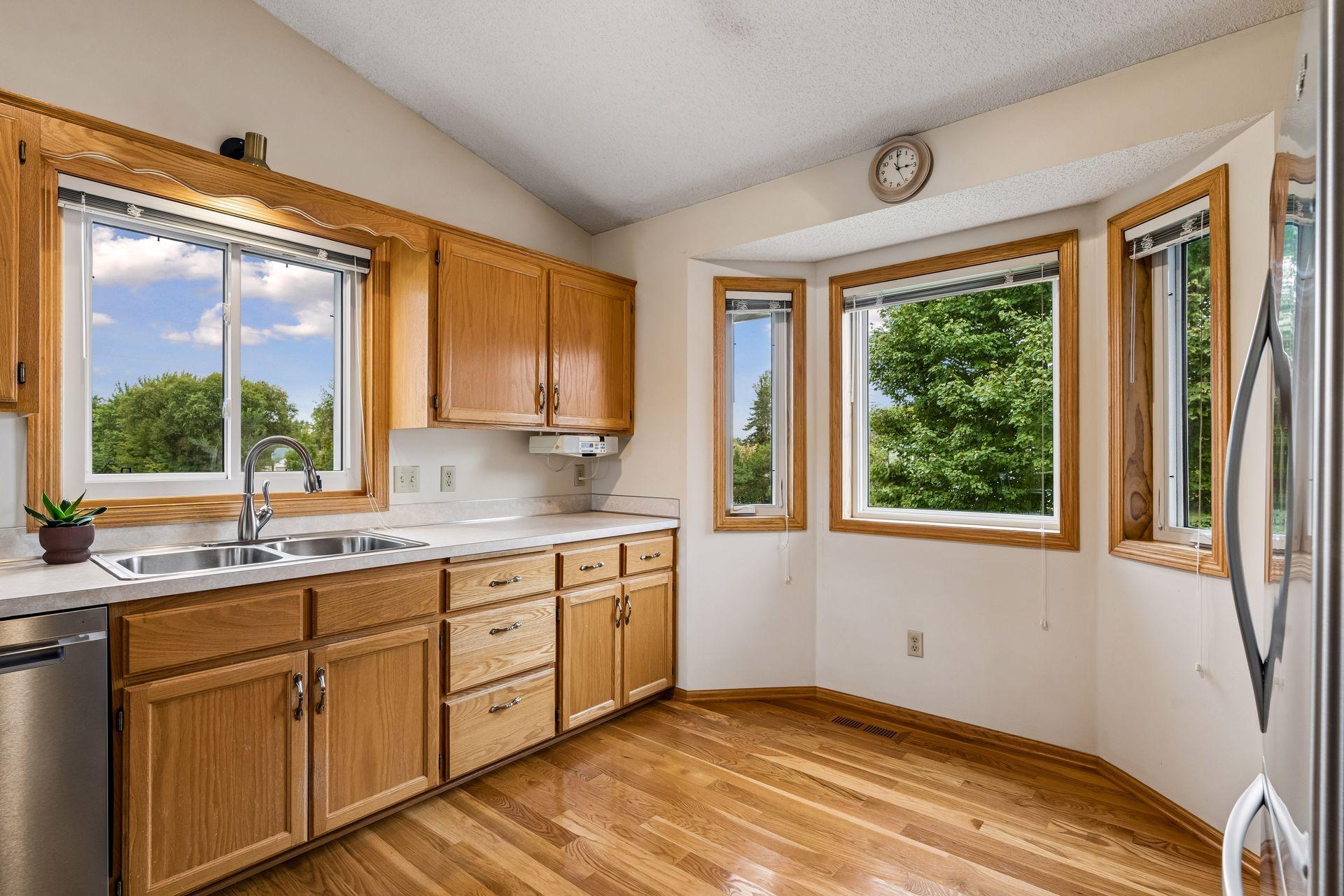Kitchen with wood cabinets, a double-basin sink, hardwood floors, and large windows overlooking trees.