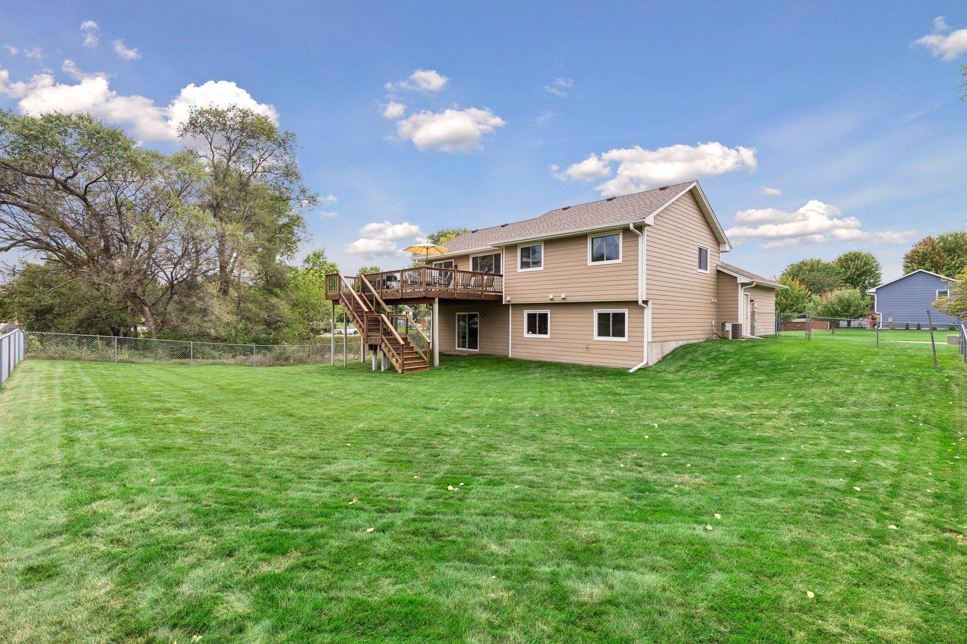 Rear of a tan two-story home with a raised deck and stairs overlooking a fenced lawn.