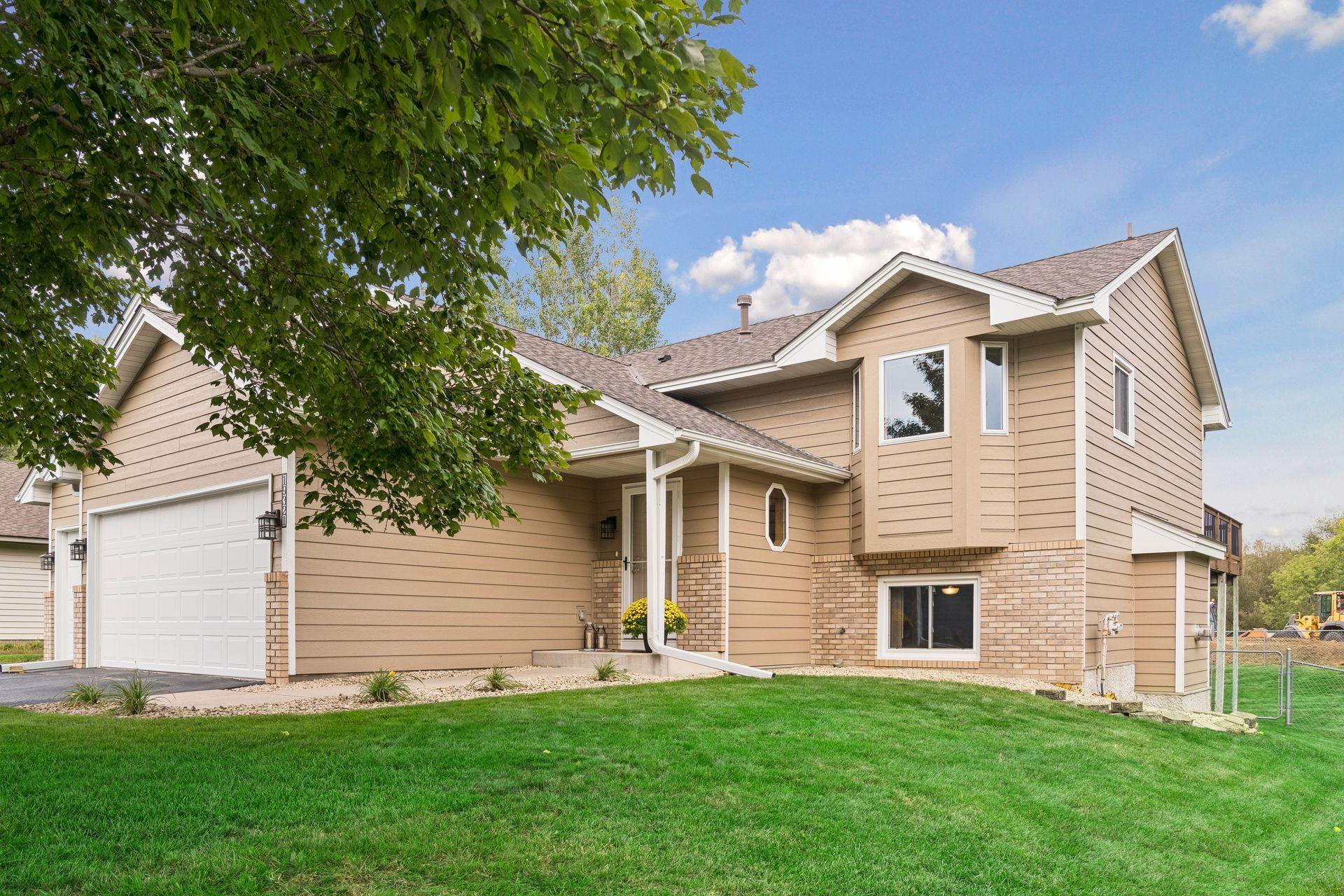 Tan two-story house with brick accents, an attached double garage, and a leafy tree in front.