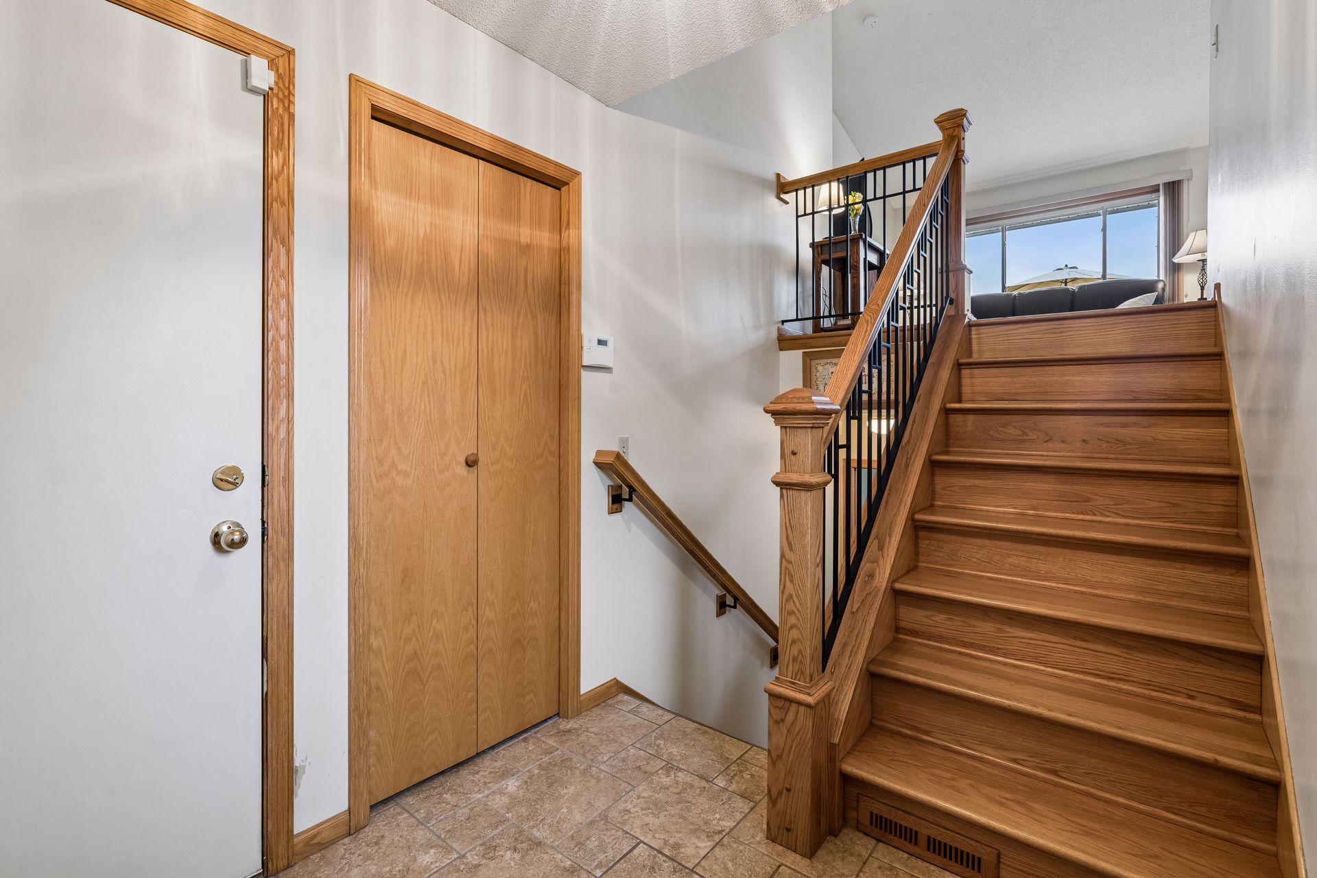 Entryway with tiled flooring, a wooden closet, and an oak staircase with black metal balusters.