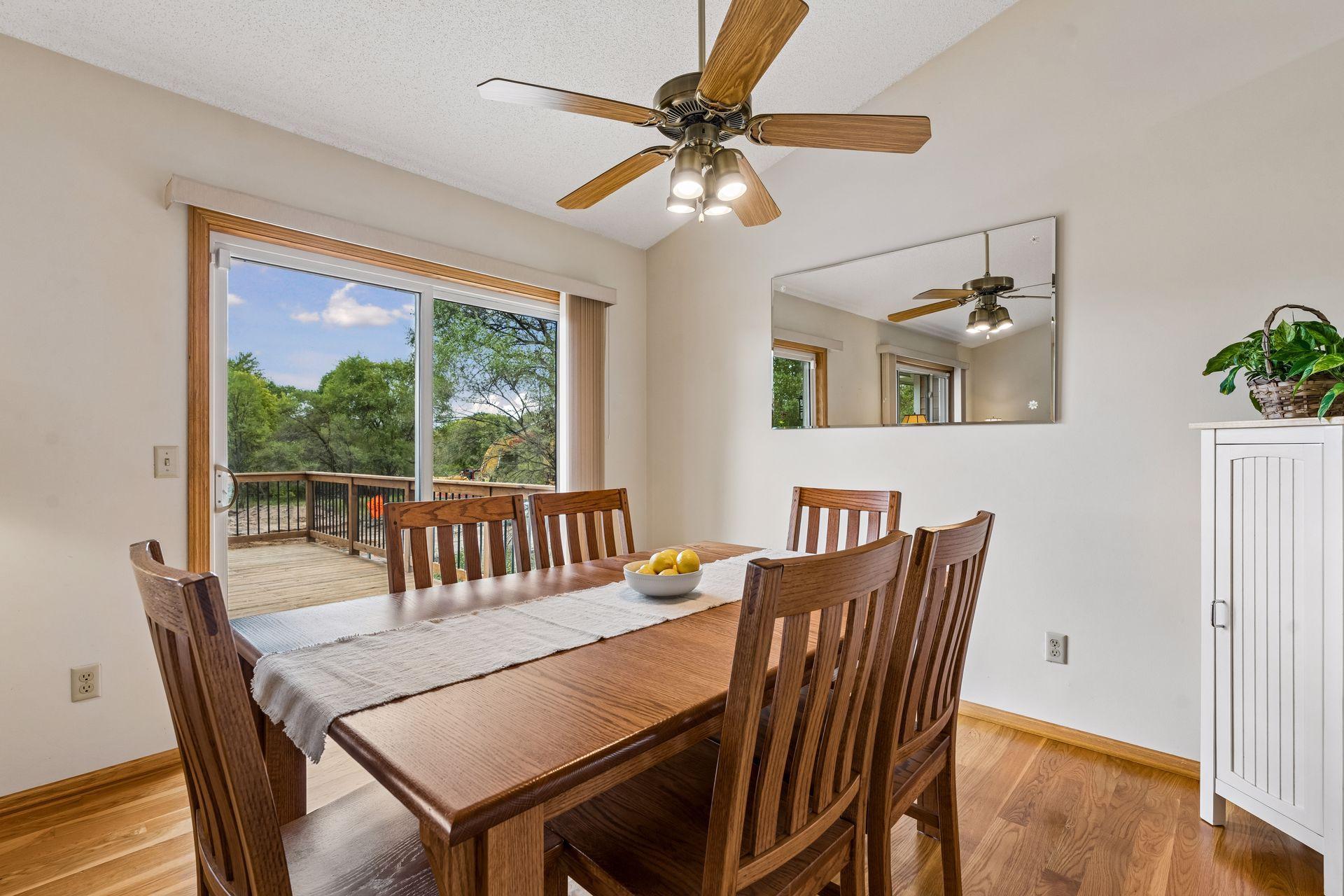 Dining room with a wooden table beside sliding doors opening onto a tree-lined deck.