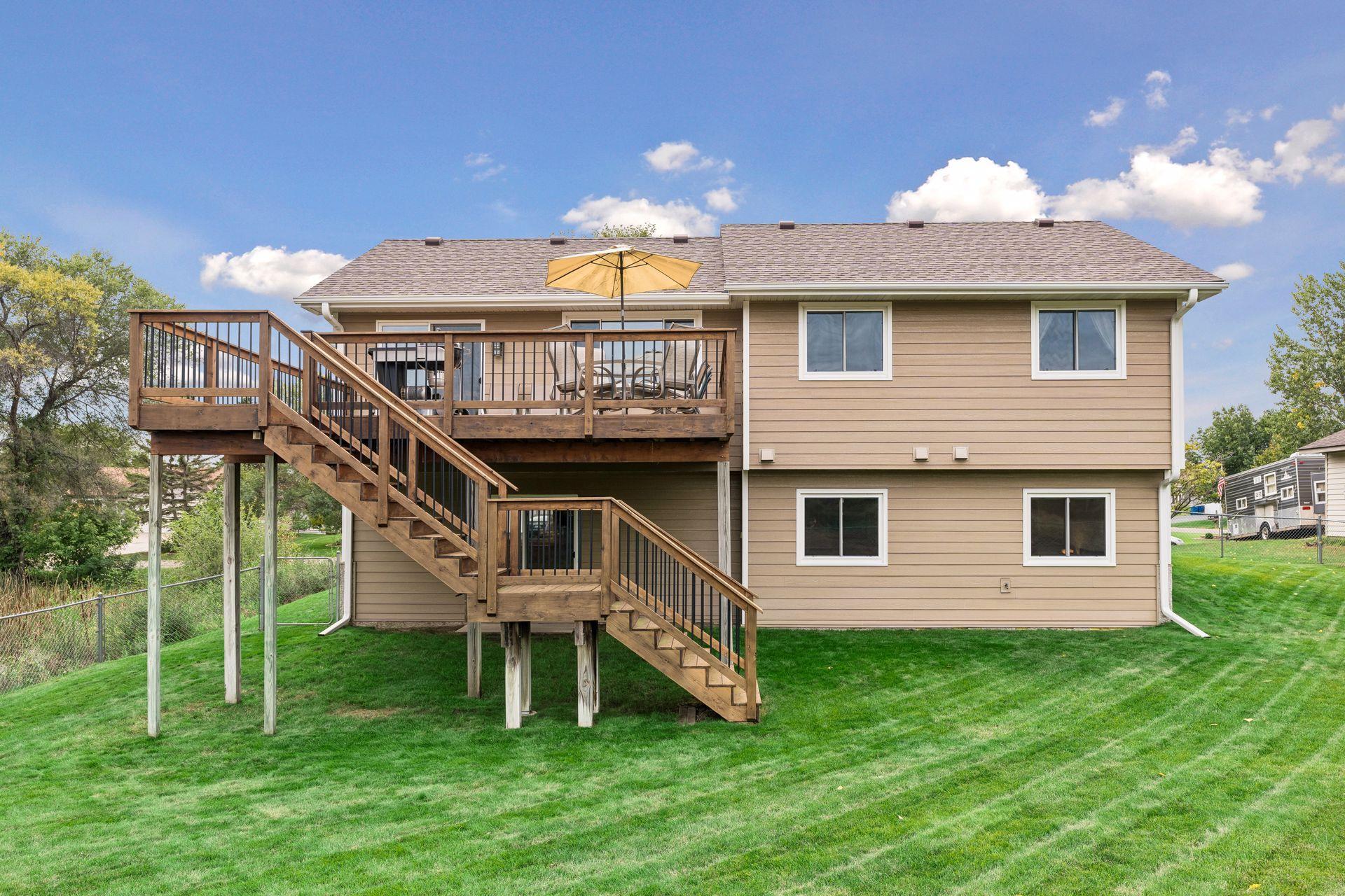House rear with a raised wooden deck, yellow umbrella, and long stairs leading to the lawn.