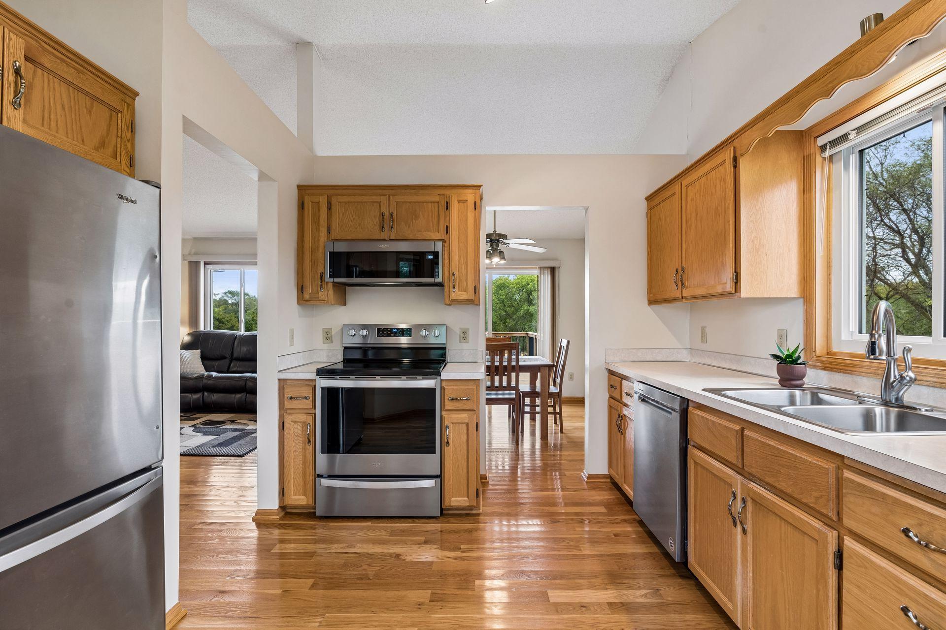 Kitchen with oak cabinets, stainless steel appliances, hardwood floors, and a large window over the sink.