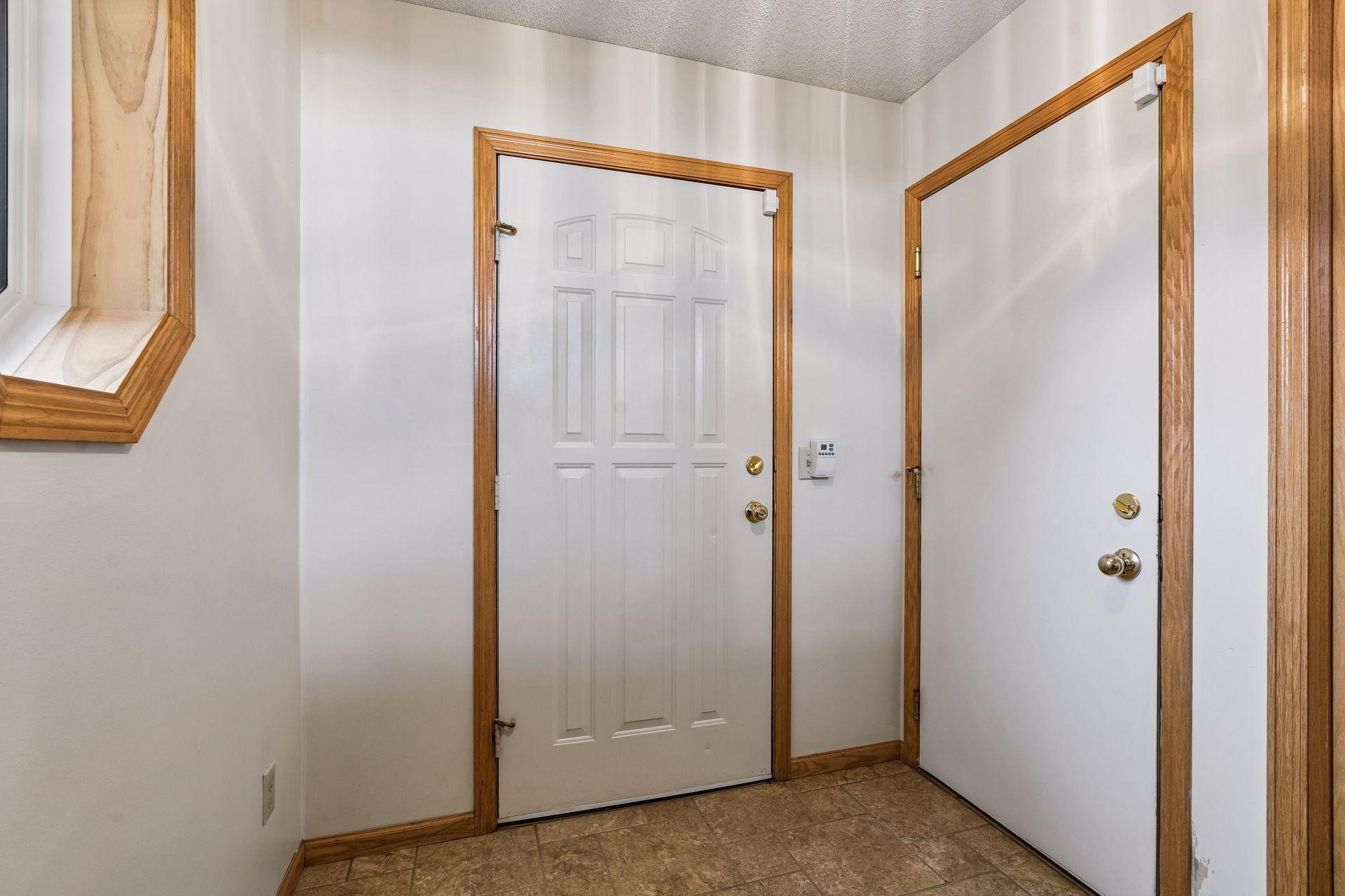 Entryway with two white doors, wood trim, and a tiled floor.