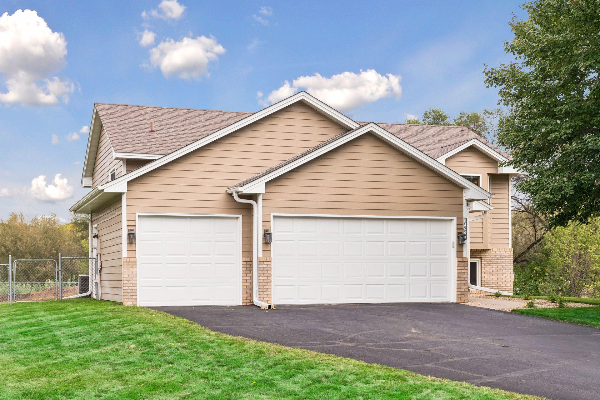 Tan two-story home with brick accents, two white garage doors, and a wide driveway.