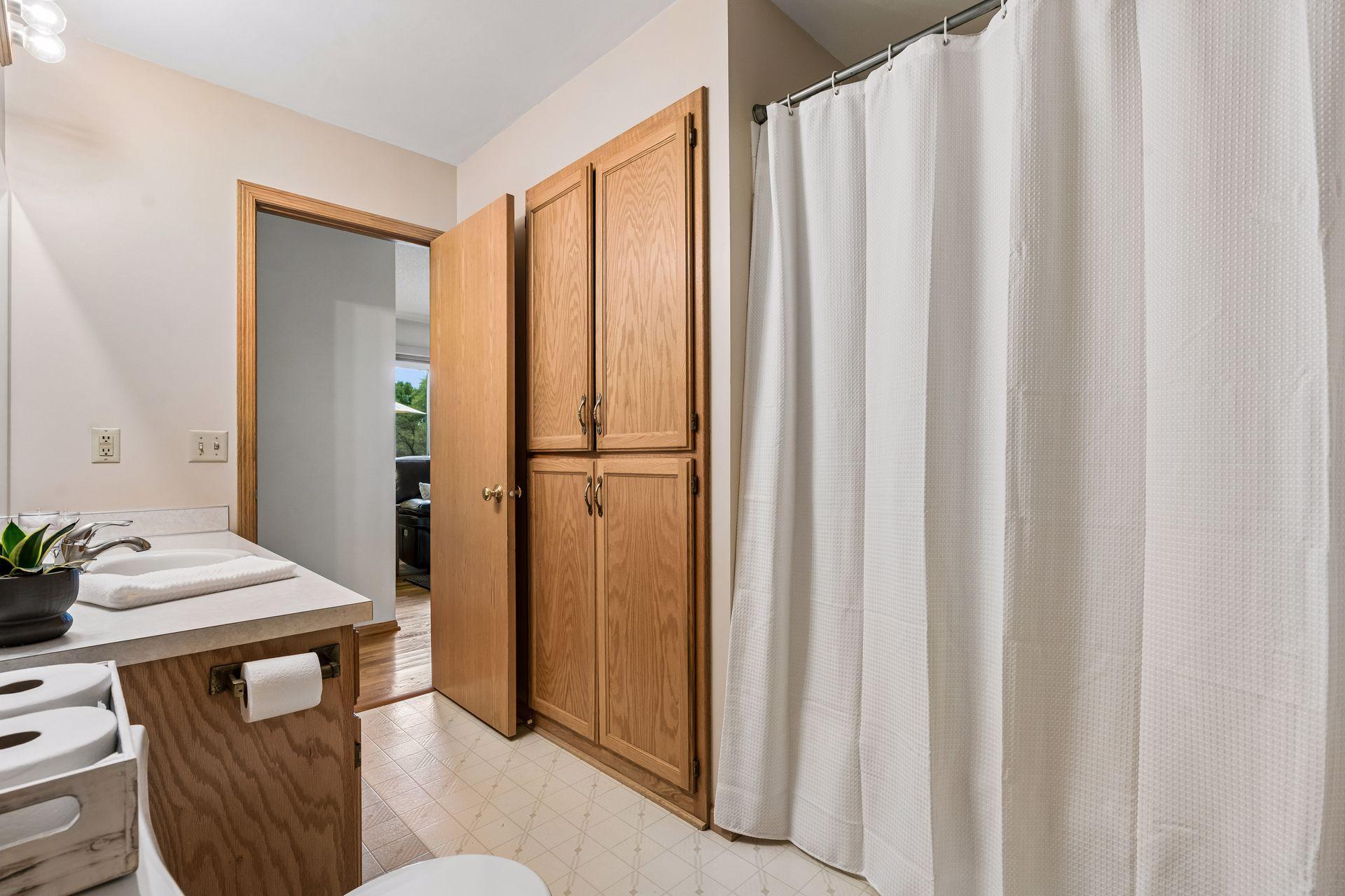 Bathroom with oak cabinetry, a white shower curtain, and a tiled floor.