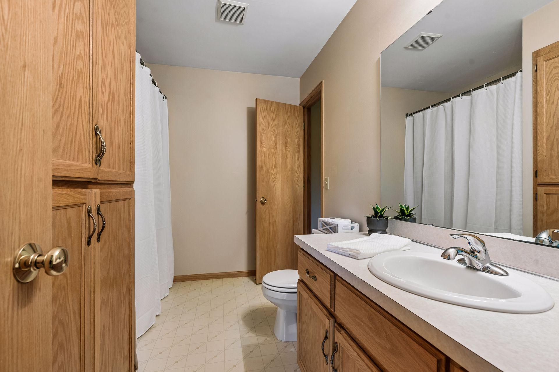 Bathroom with an oak vanity, large mirror, white countertop, and shower curtain.