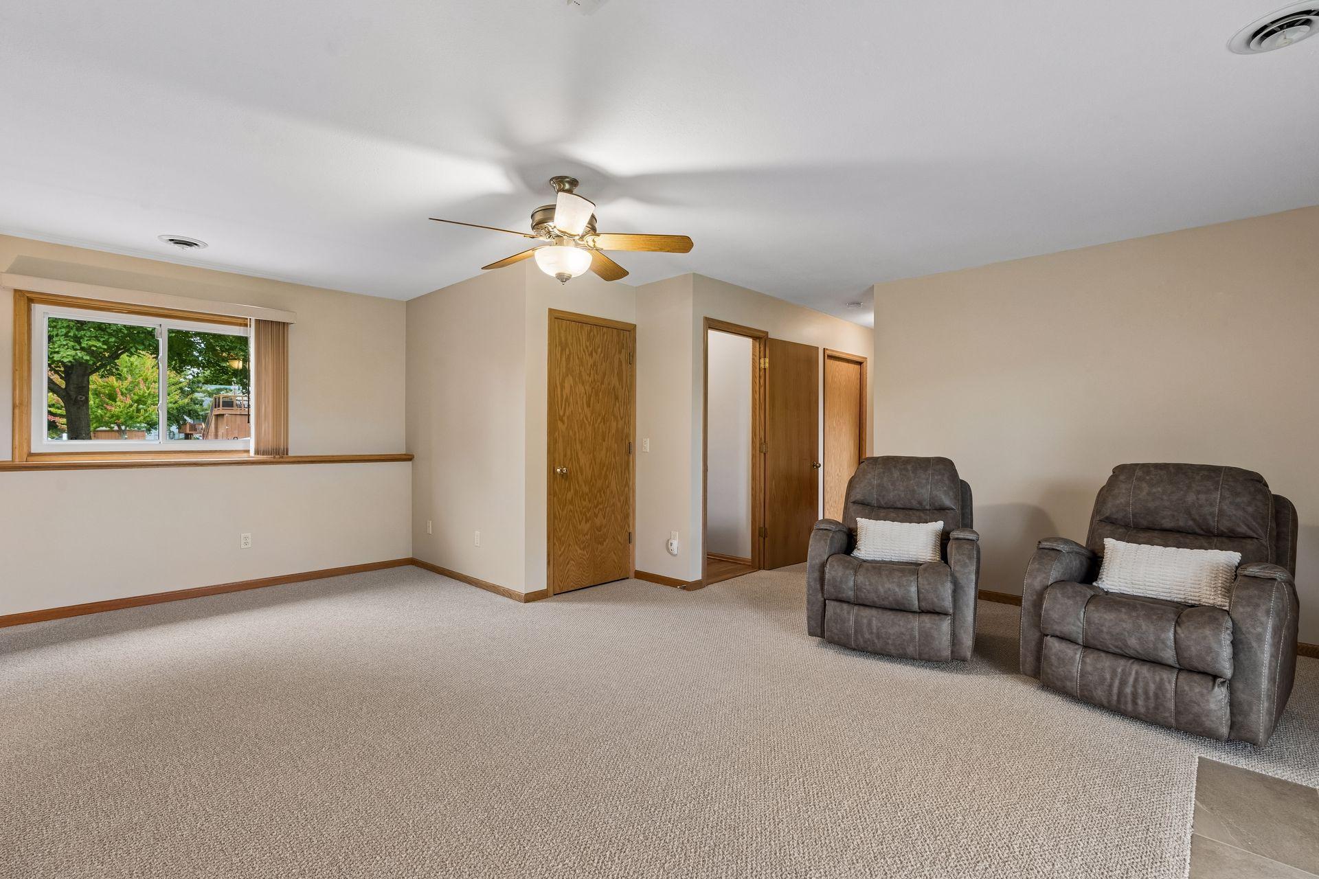 Carpeted living room with two gray recliners, a wood-trimmed window, and a ceiling fan.