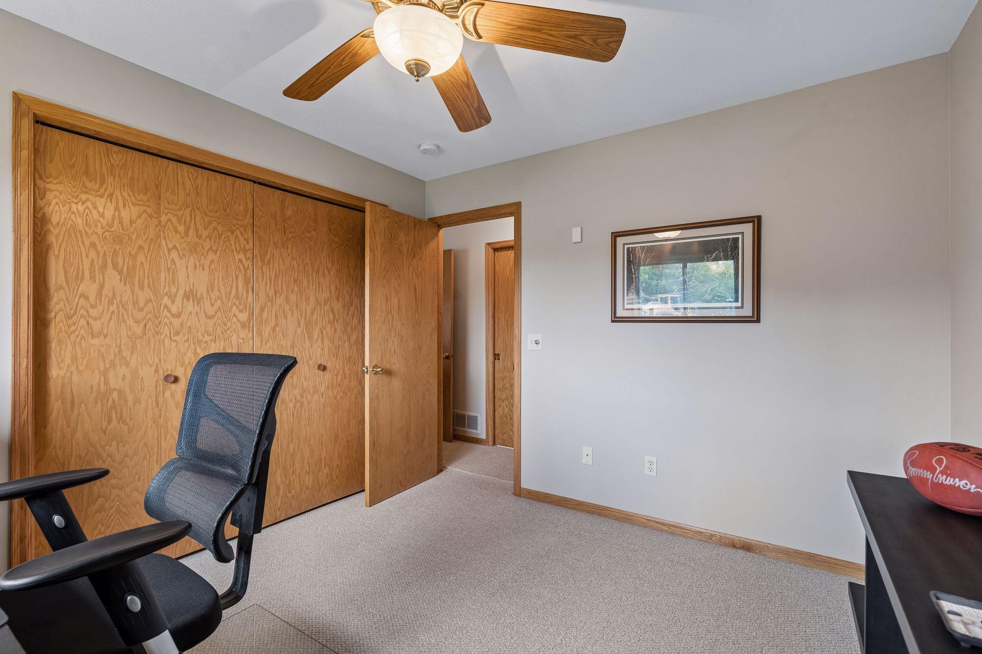 Carpeted home office with wooden sliding closet doors and a ceiling fan.