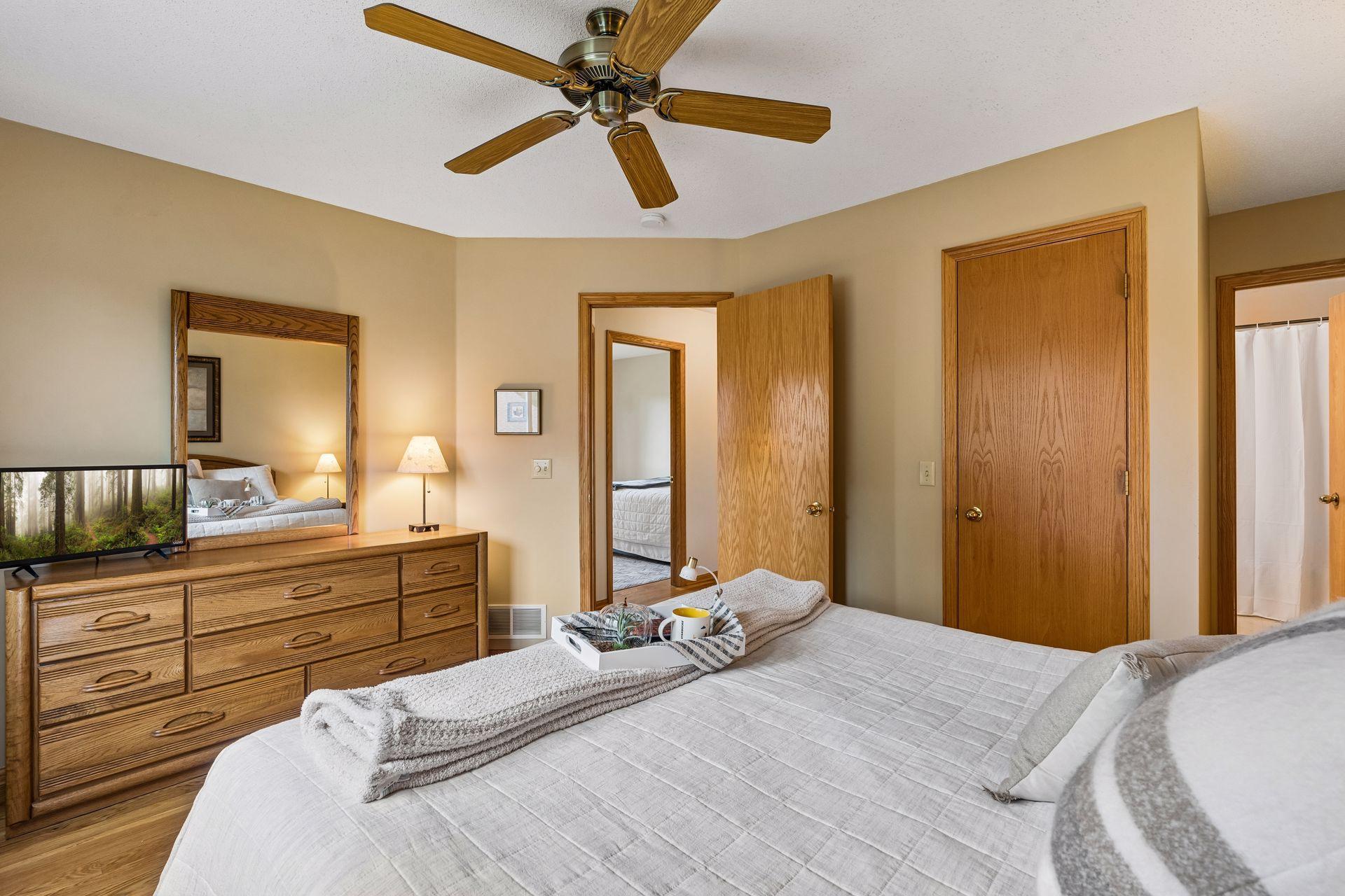 Furnished bedroom with a large bed, wood dresser, and ceiling fan.