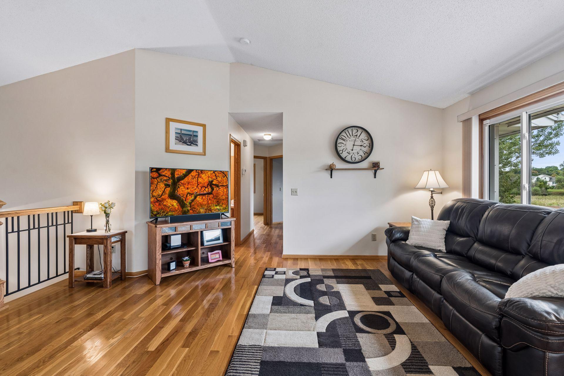 Living room with black leather sofa, patterned rug, hardwood floors, and sliding glass doors.