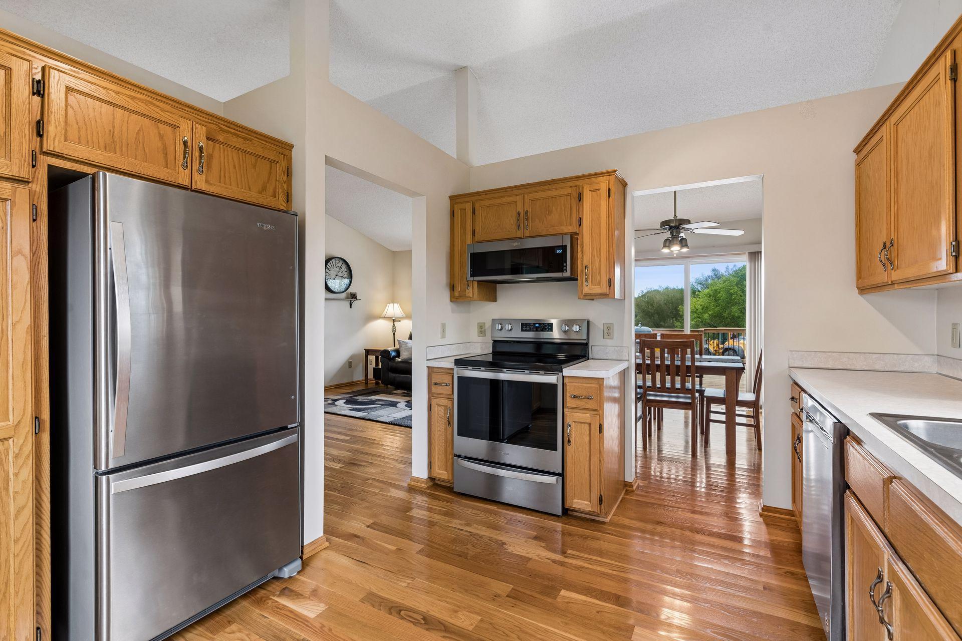 Kitchen with wood cabinets, stainless steel appliances, and an adjoining dining area overlooking greenery.