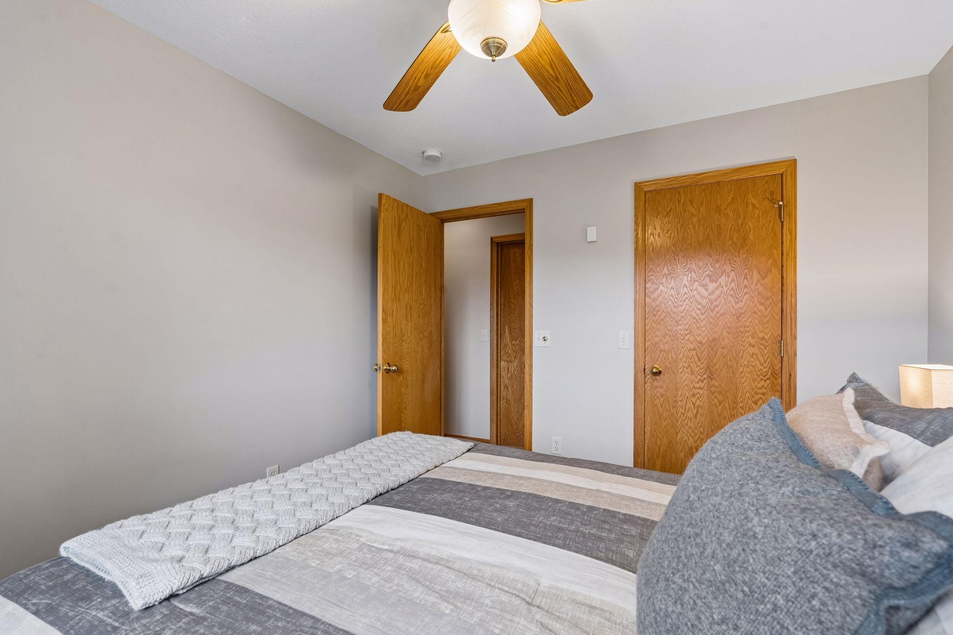 Bedroom with gray striped bedding, a knitted throw, and warm wood doors.