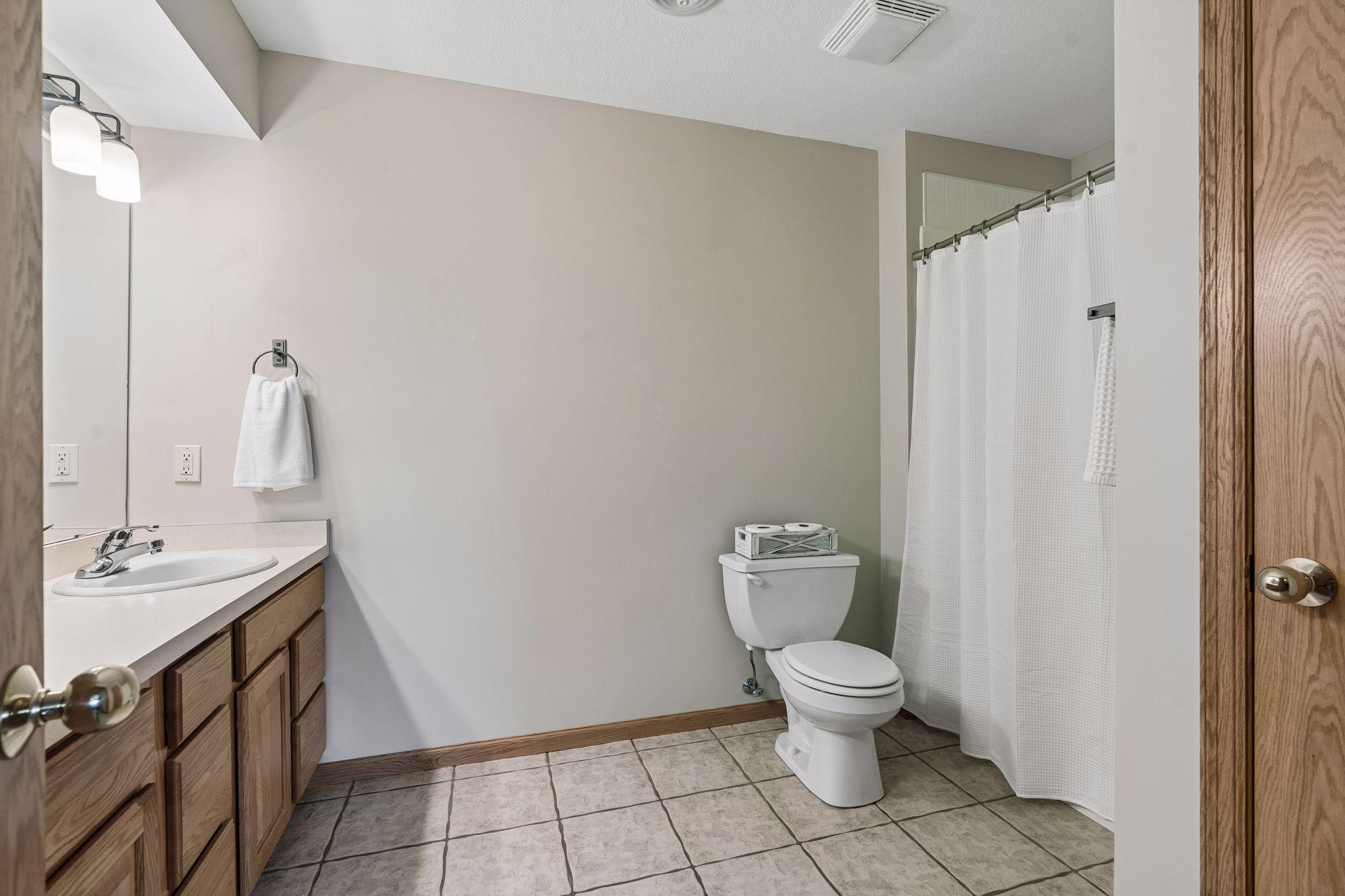 Bathroom with a wood vanity, tiled floor, and shower behind a white curtain.