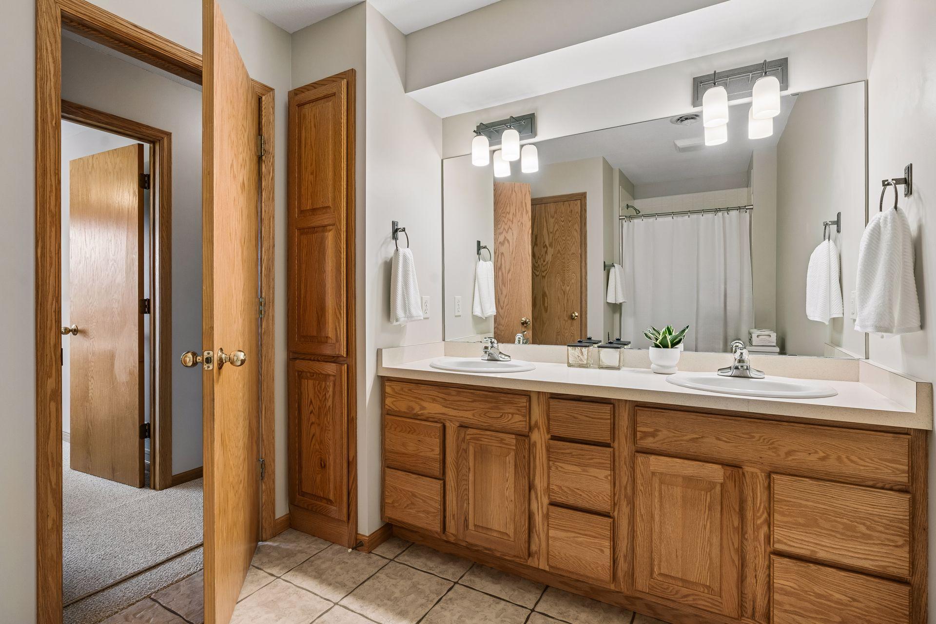 Bathroom with a double-sink vanity, oak cabinetry, and a large mirror reflecting the shower.