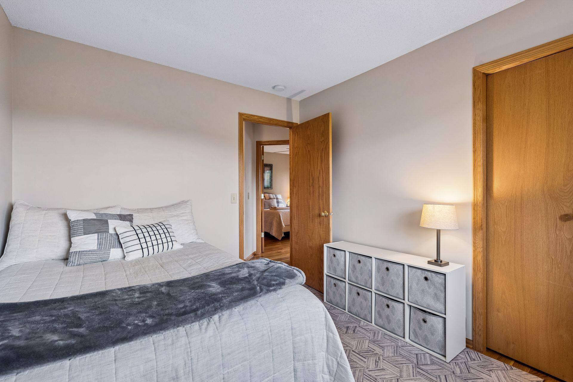 Furnished bedroom with a gray bed, white cubby storage, and an open doorway to another bedroom.